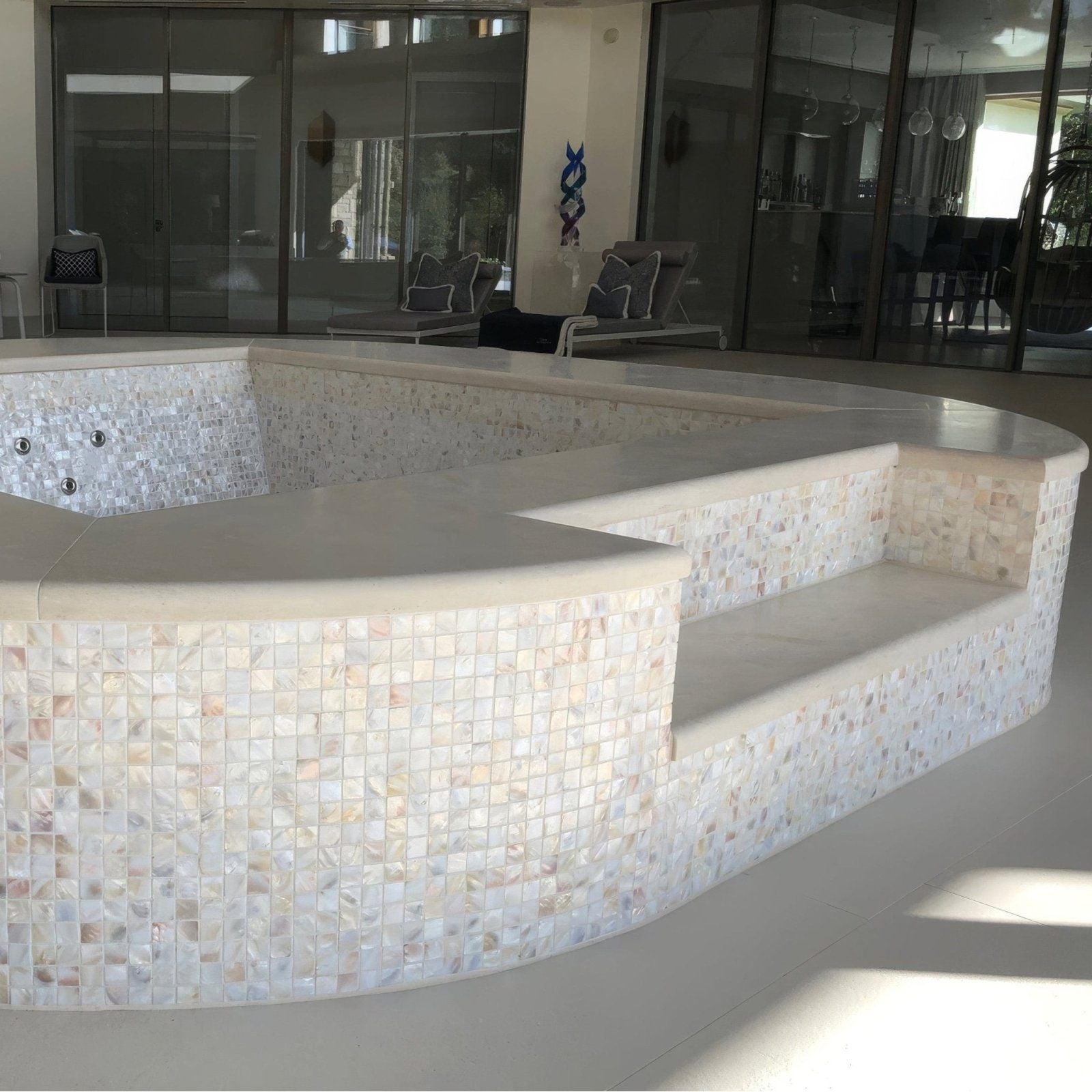 A curved multi-tiered hot tub with smooth beige concrete and iridescent white mother-of-pearl mosaic tiles natural 25mm square