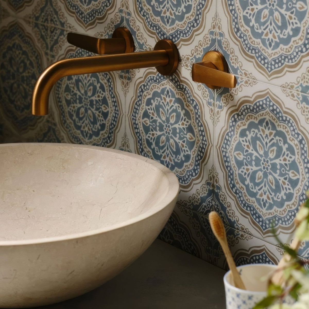 Brass wall-mounted faucet with curved spout and rectangular handles installed on nina campbell udaipur blue porcelain tile