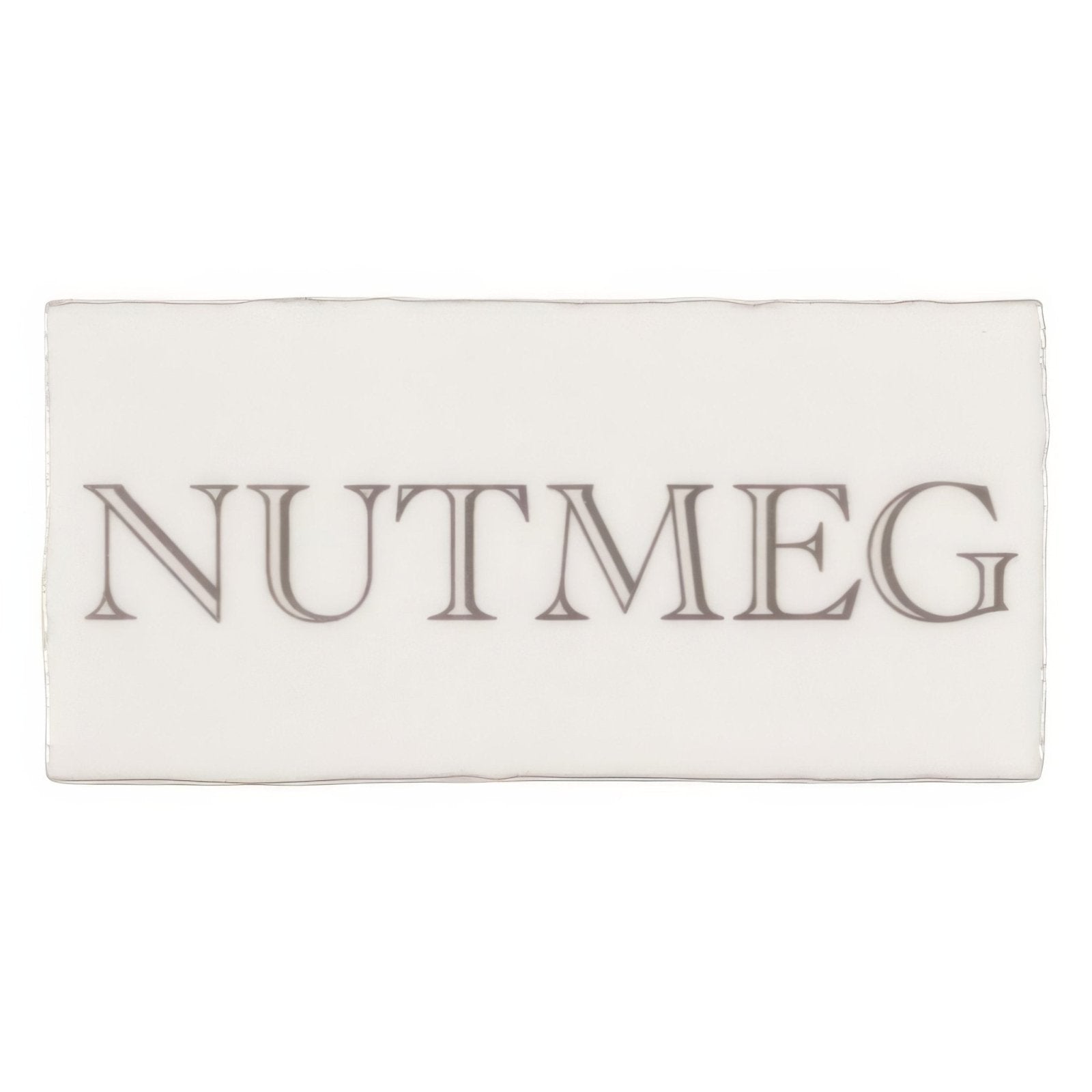 A rectangular white ceramic tile embossed with nutmeg in dark gray serif font from nutmeg in grey on cotton