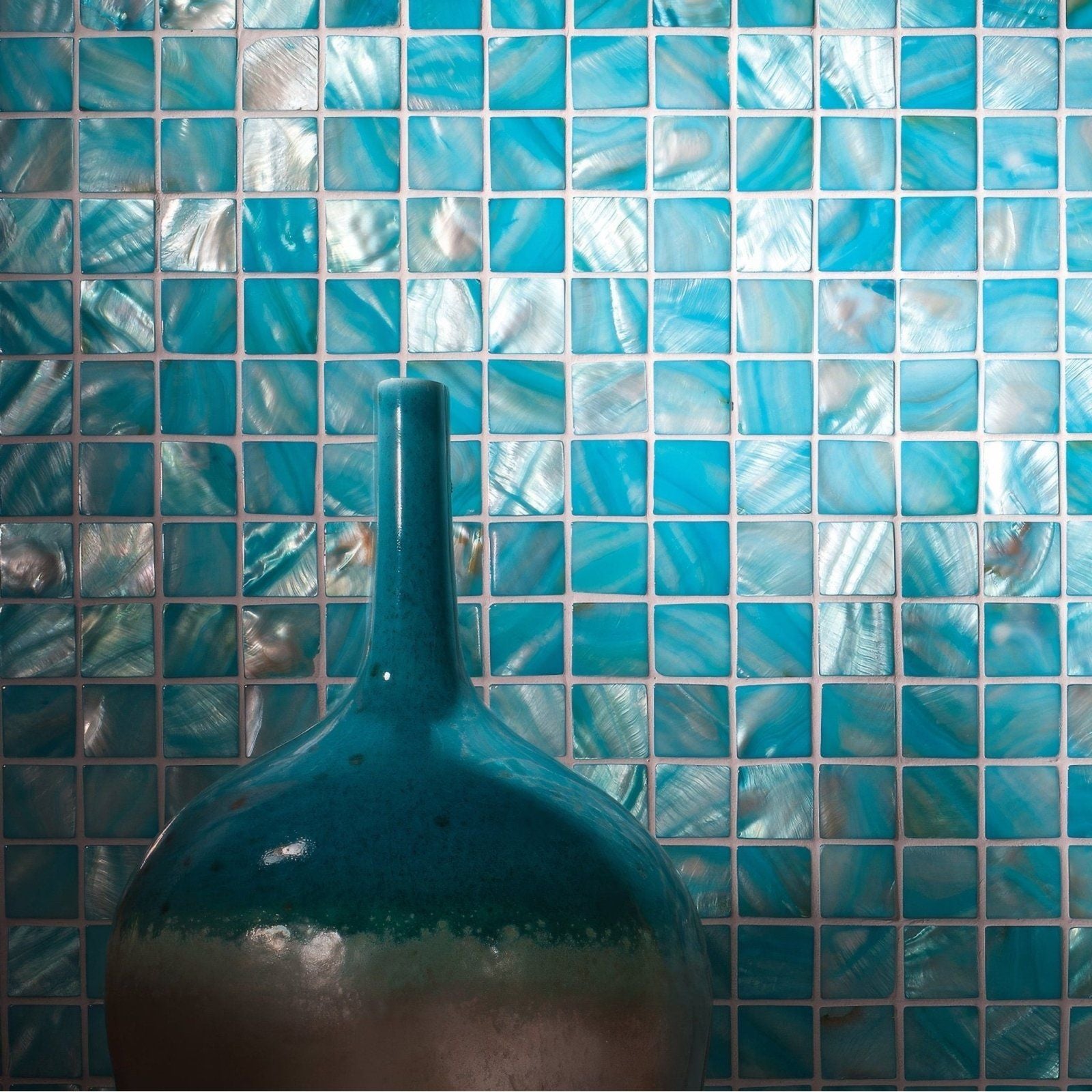 A glossy teal ceramic vase with slender neck and rounded body against shimmering blue mosaic tiles ocean’s calm 25mm square