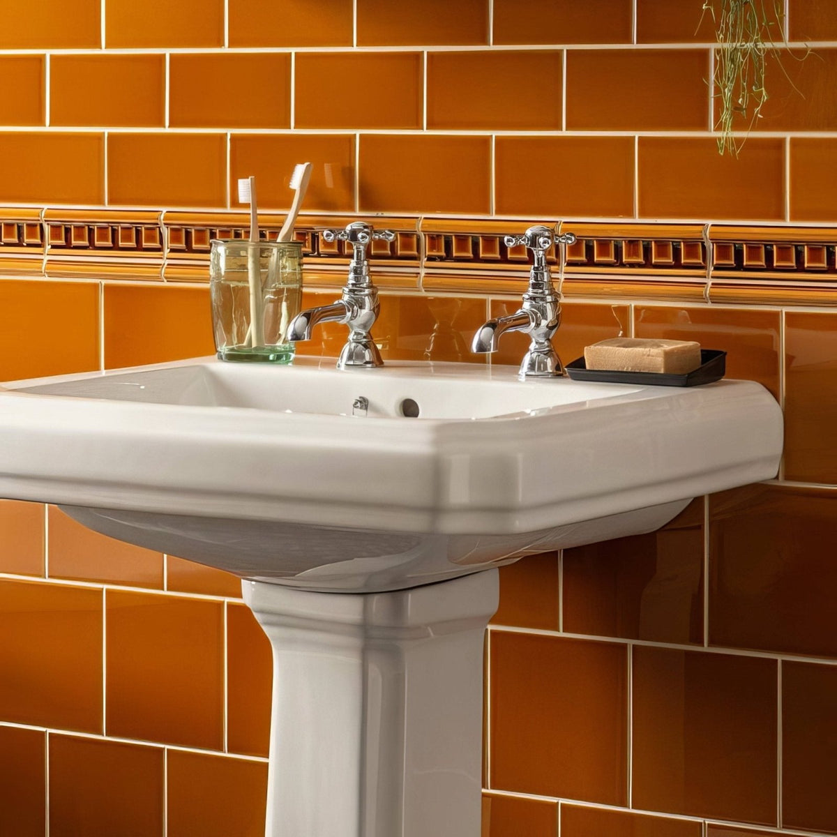 White ceramic pedestal sink with chrome faucets showcased with ochre half tile background for bathroom use