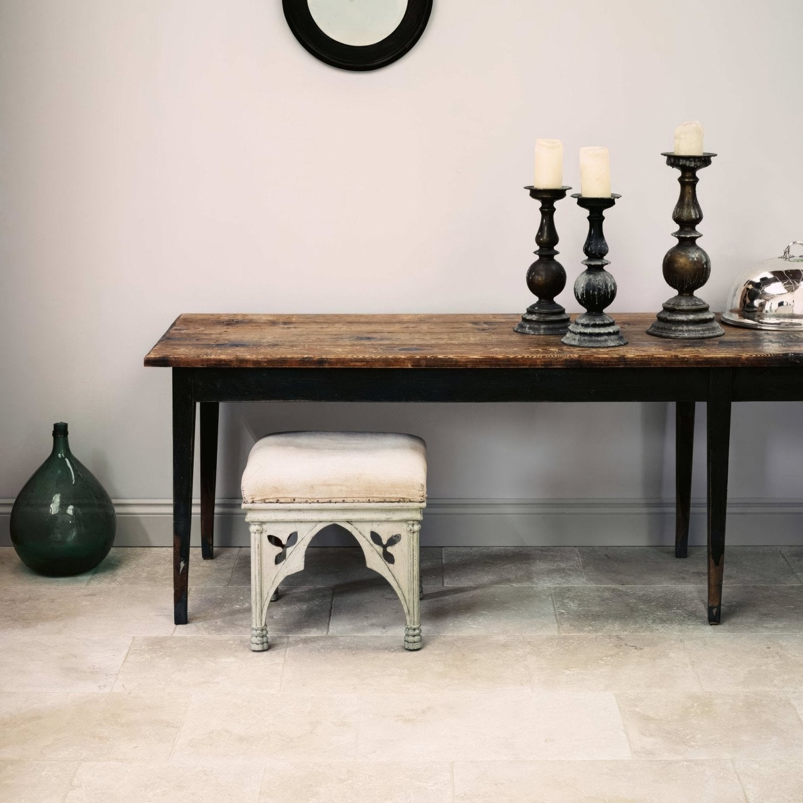 A distressed white painted gothic style stool with cream upholstered seat featuring decorative leaf motifs on legs