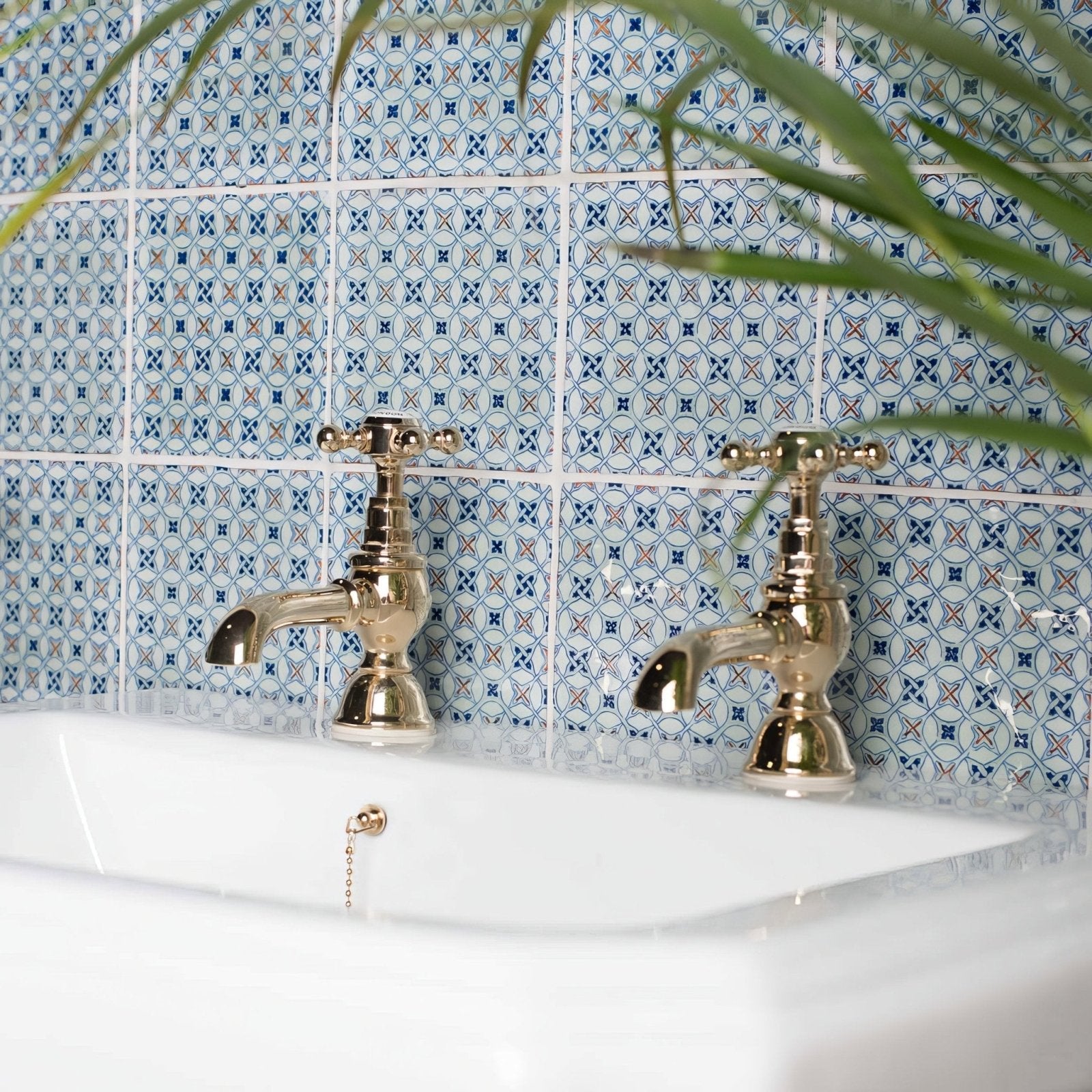 Vintage-style brass-finished ormeaux red on mint bathroom taps with cross handles on a white sink and blue white tiles