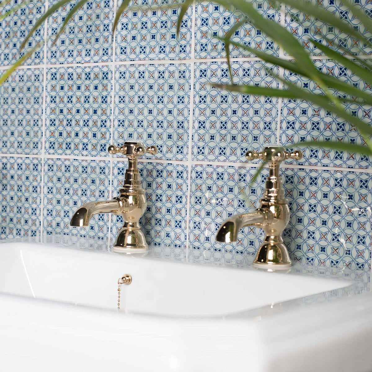 Vintage-style brass-finished ormeaux red on mint bathroom taps with cross handles on a white sink and blue white tiles