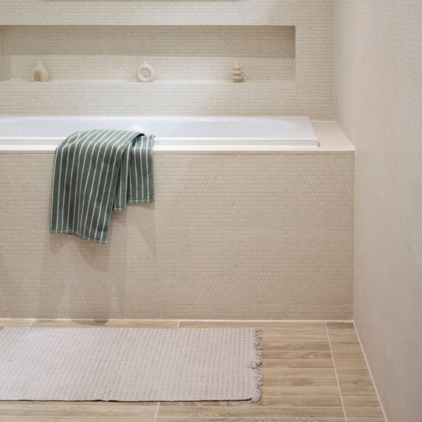 A green and white striped towel draped over the edge of a bathtub with palio limestone brick mosaic tile background