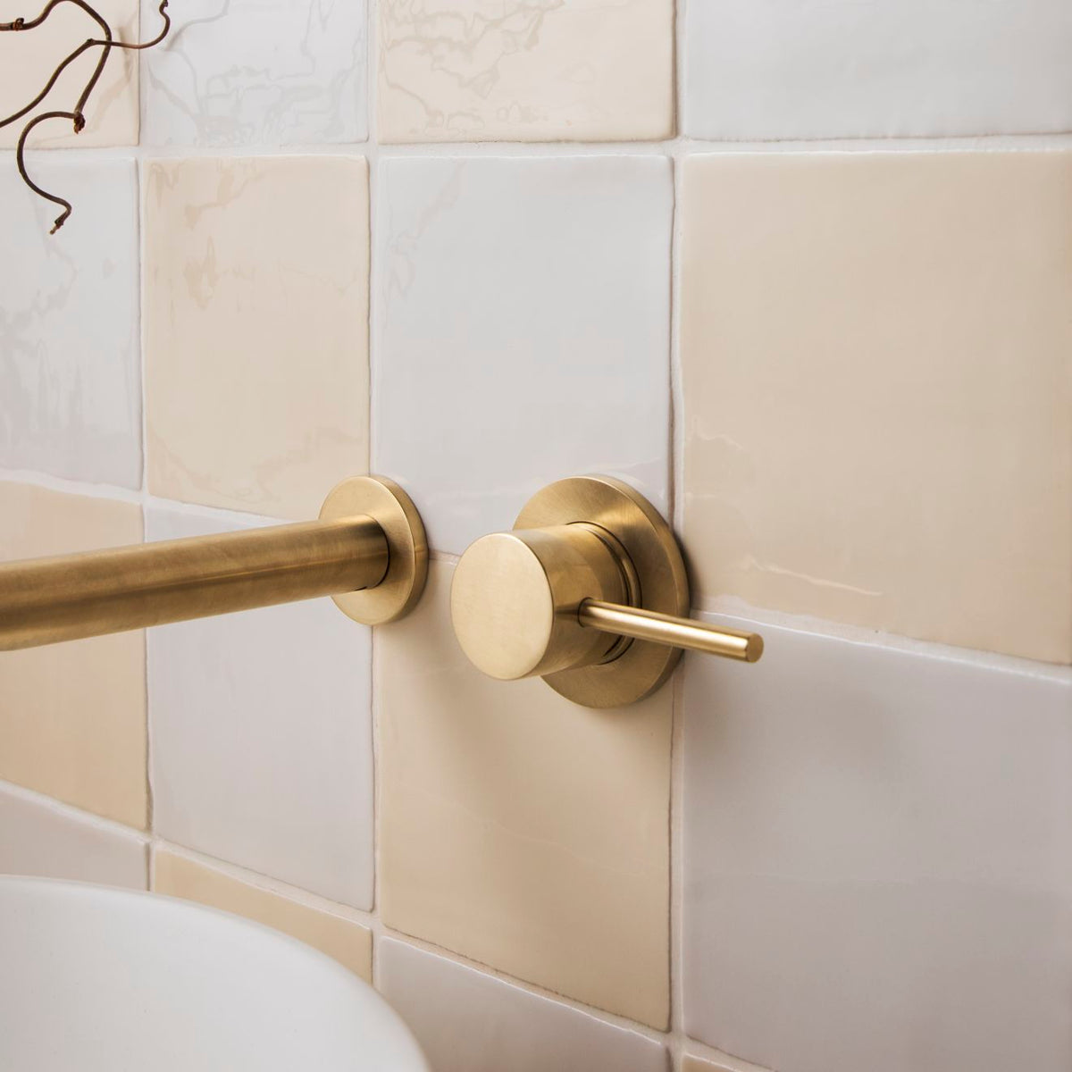 Brass-finished wall-mounted faucet with sleek cylindrical spout and circular handle in palomino field tile setting