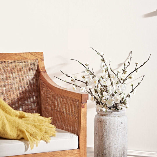 A tall textured gray ceramic vase with a bouquet of delicate white blossoms on dark branches called passion flower