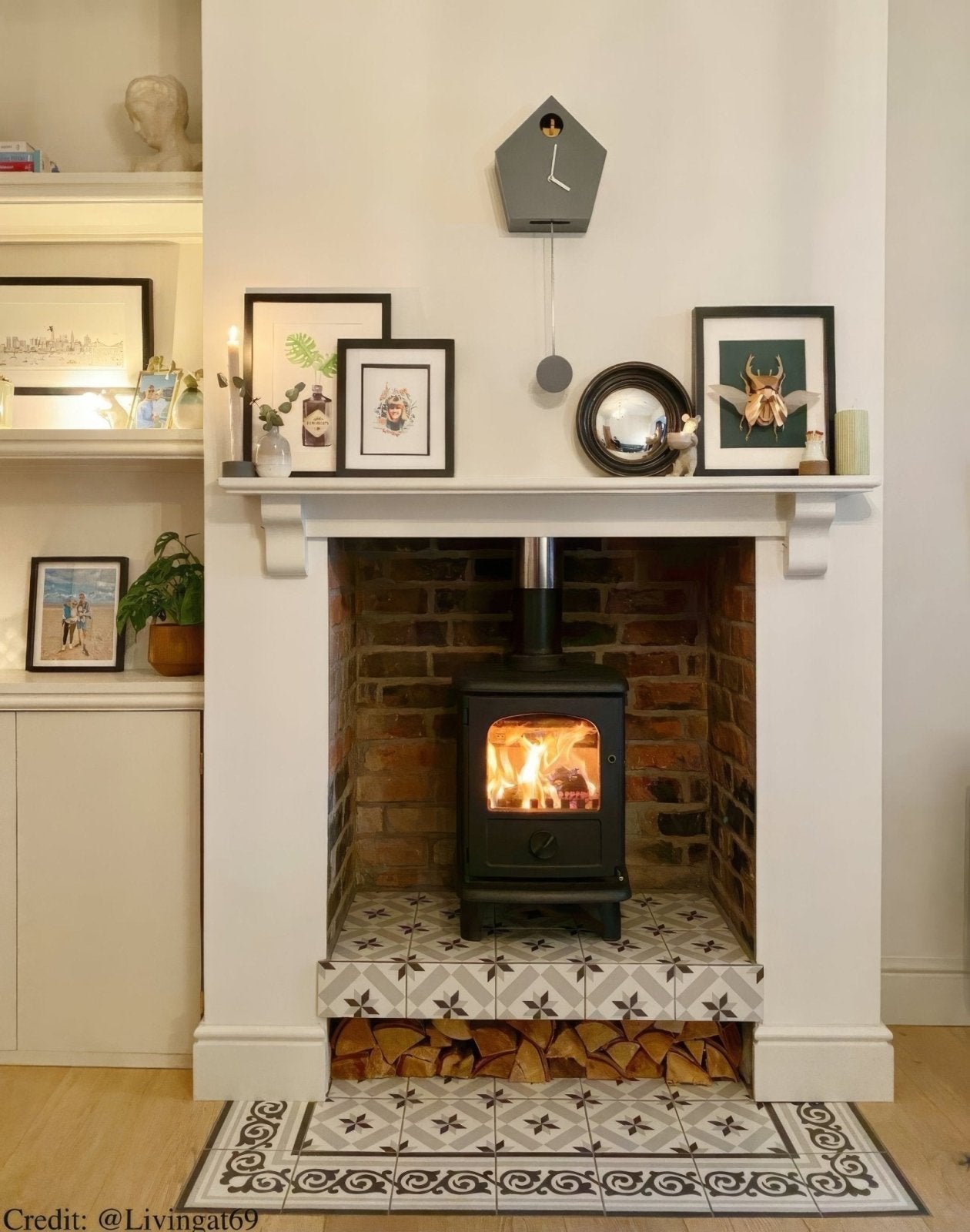 Wood-burning stove in a fireplace with Patisserie Sucre 1 Patterned Tile decorative elements and framed pictures.