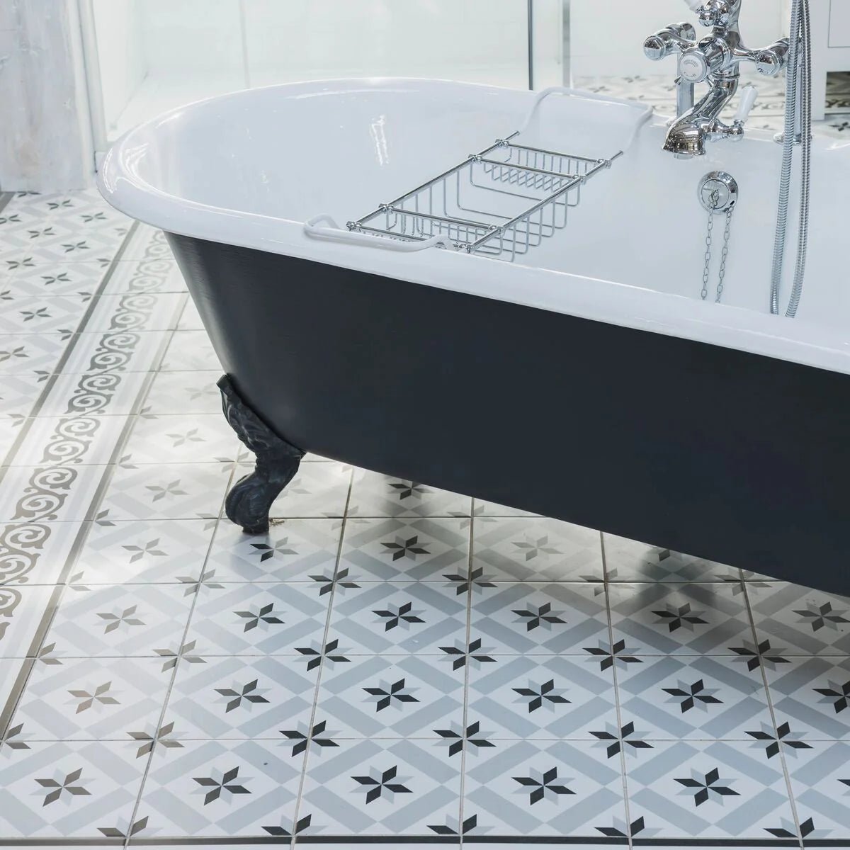 Black and white clawfoot bathtub with chrome fixtures against patisserie sucre 1 patterned tile wall