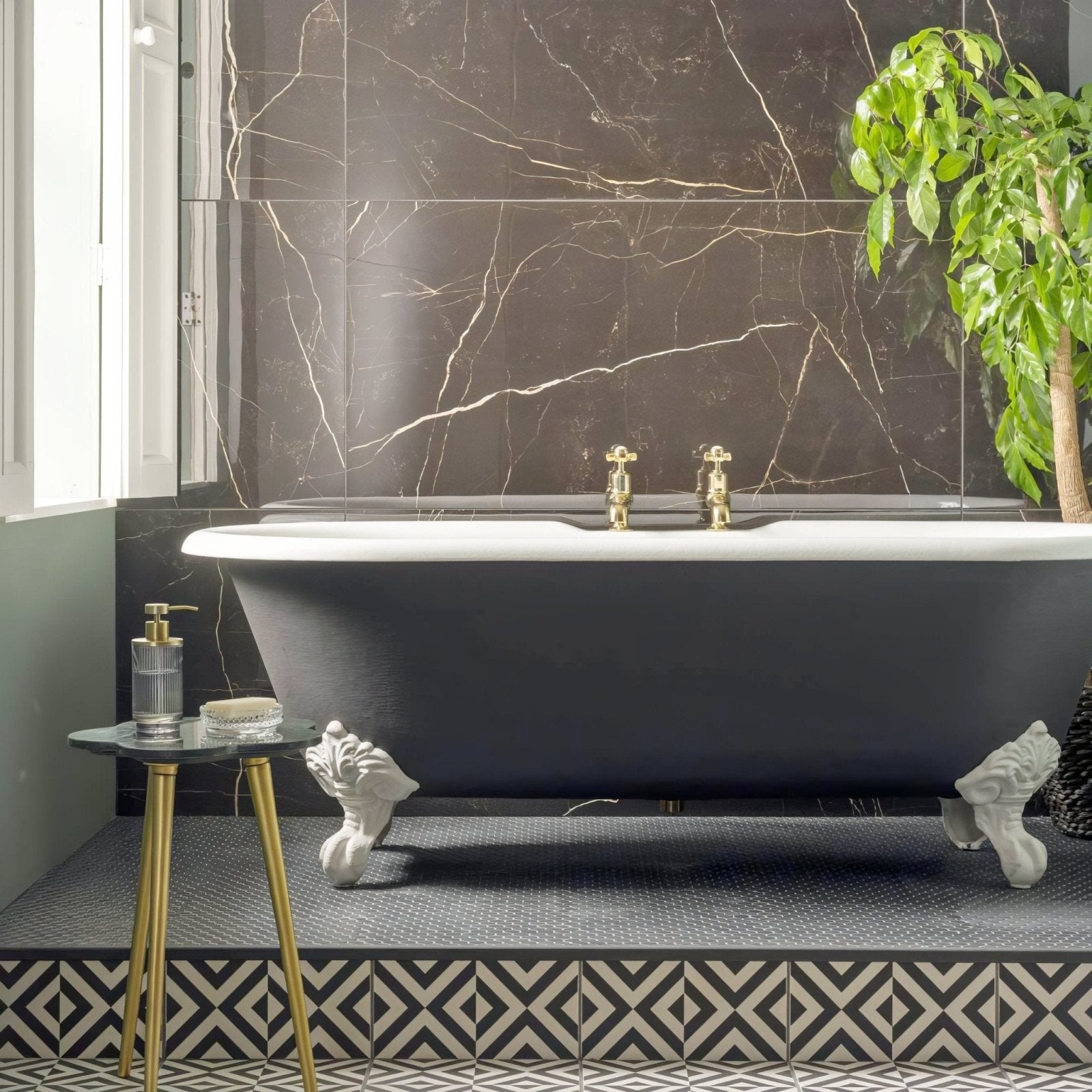 Black clawfoot bathtub with gold fixtures against white marble patterned walls in penshaw black on chalk finish