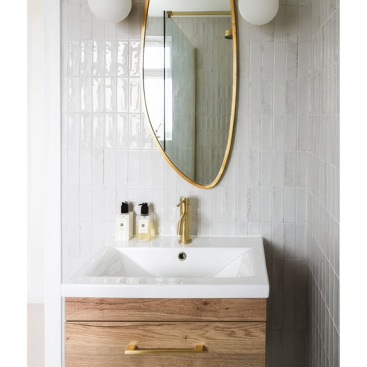 Petite porcelain gloss white sink with wooden cabinet and brass fixtures under a gold-framed oval mirror