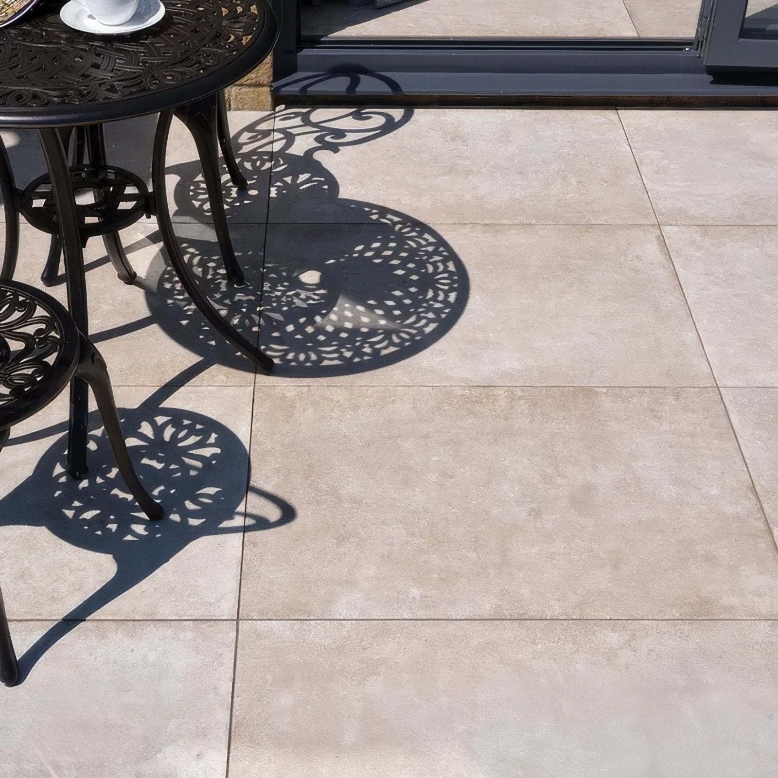 Black wrought iron patio table with intricate scrollwork design on pierre porcelain paving beige surface