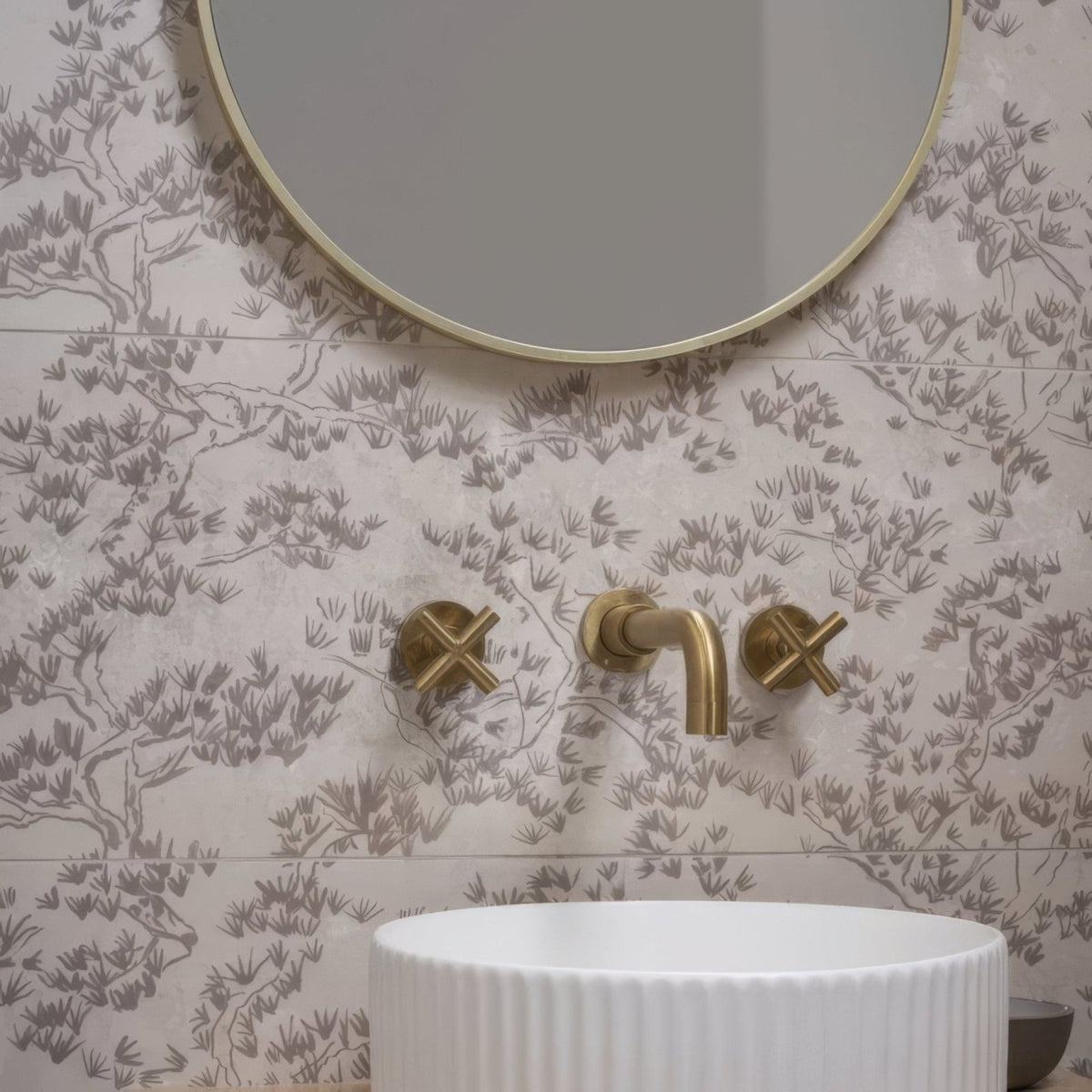 Gold-finished wall-mounted faucet with cross handles and curved spout against patterned eastern mist pine single tile wallpaper