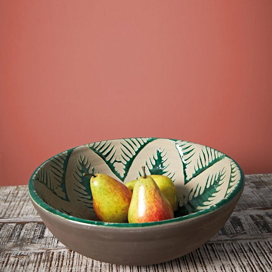A ceramic bowl pompeiian red with gray exterior and white interior decorated with green fern patterns holding three pears