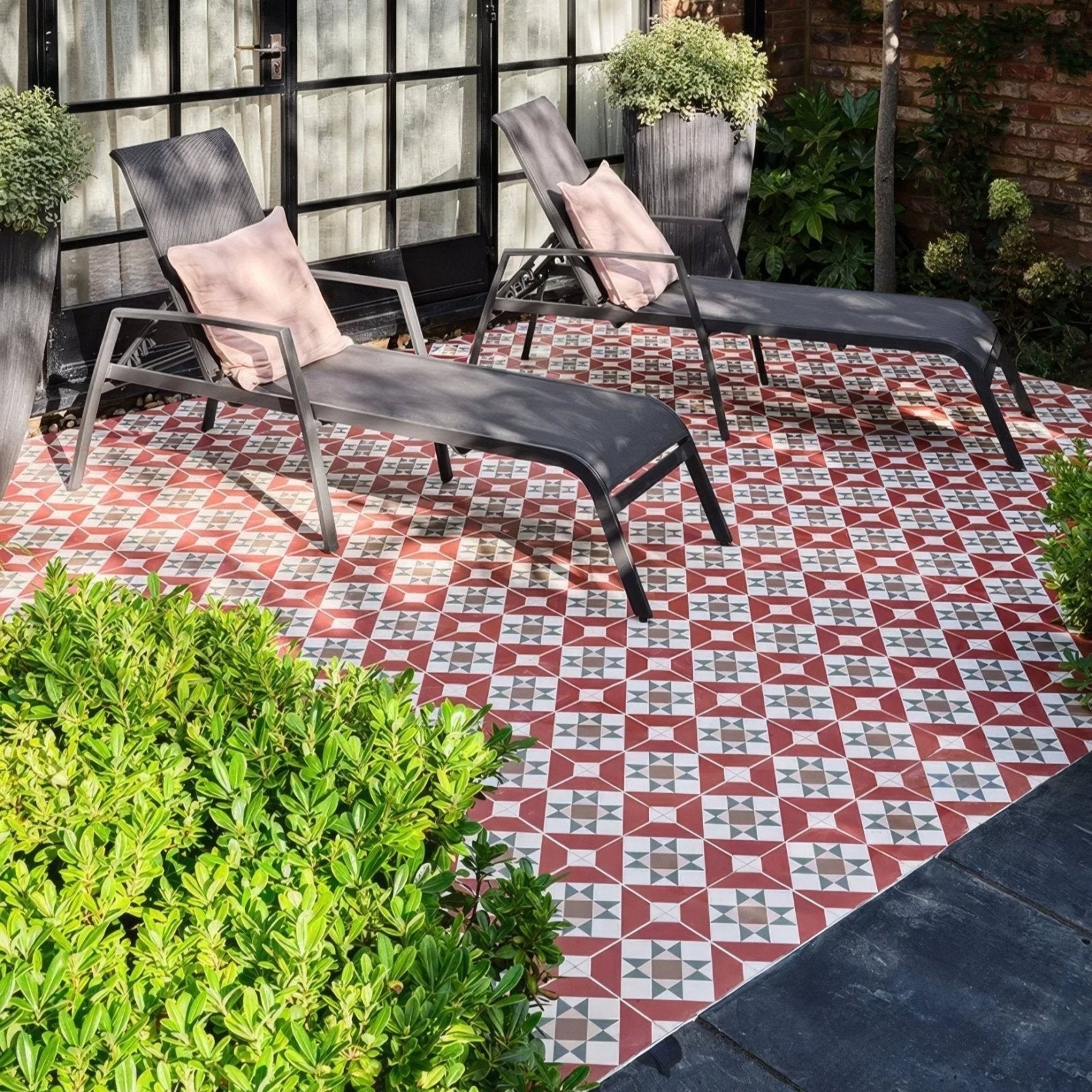 Black metal-framed brompton porcelain clarence lounge chairs with pink cushions on geometric patio tile