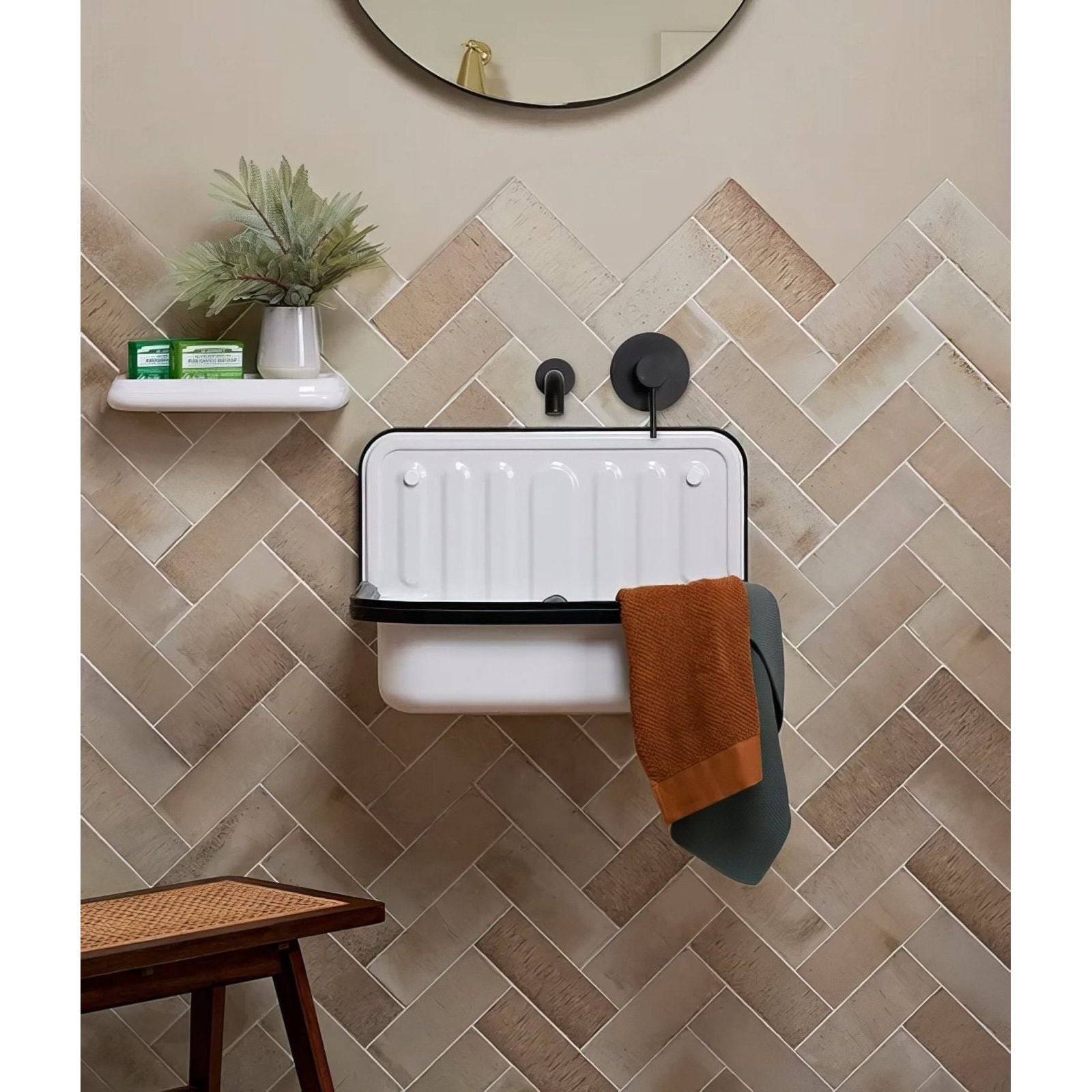 White enamel farmhouse sink with black rim and vertical ridges mounted on herringbone oatmeal brick porcelain tile wall