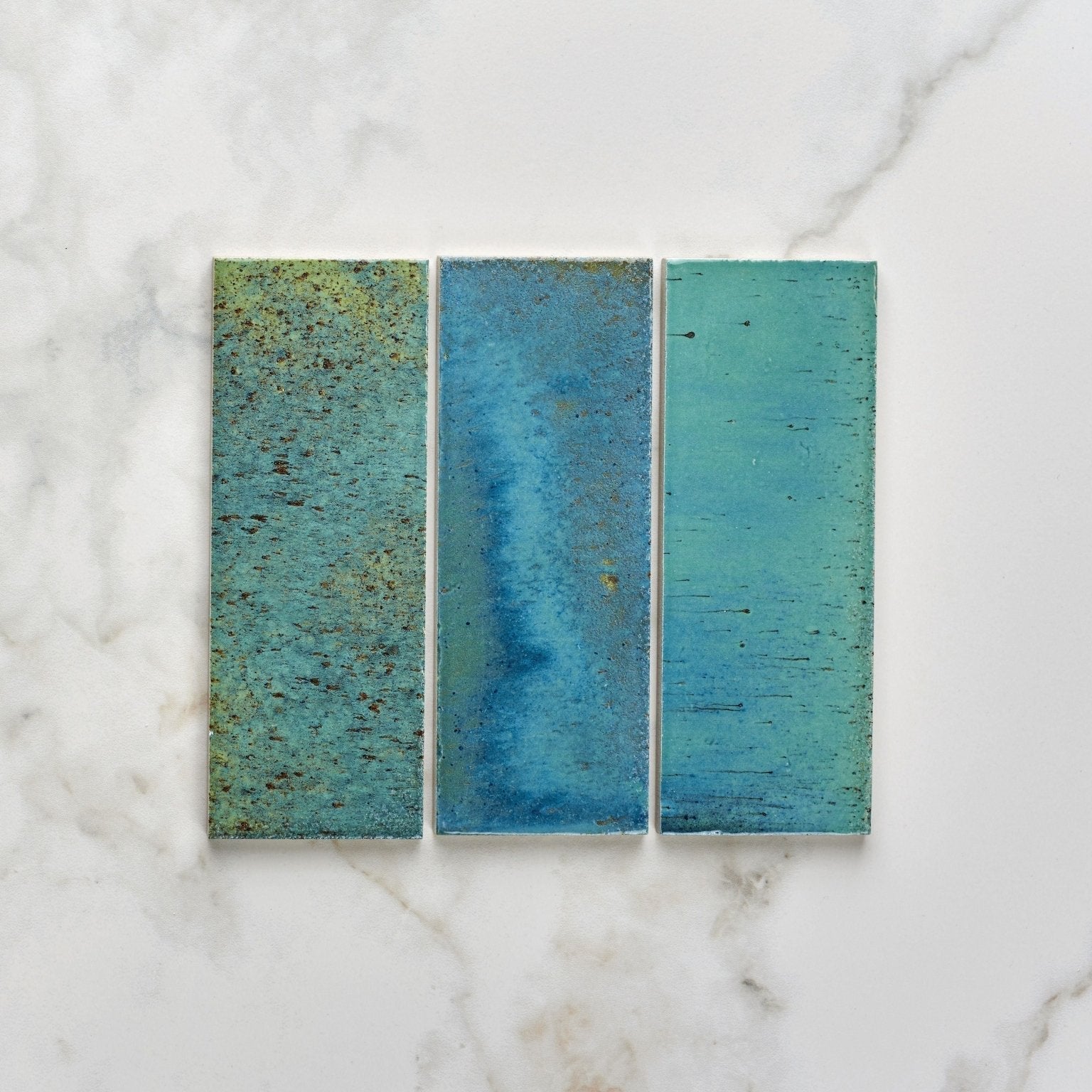 Three rectangular pottery porcelain ocean blue brick tiles with textured glazed surfaces in shades of teal and blue