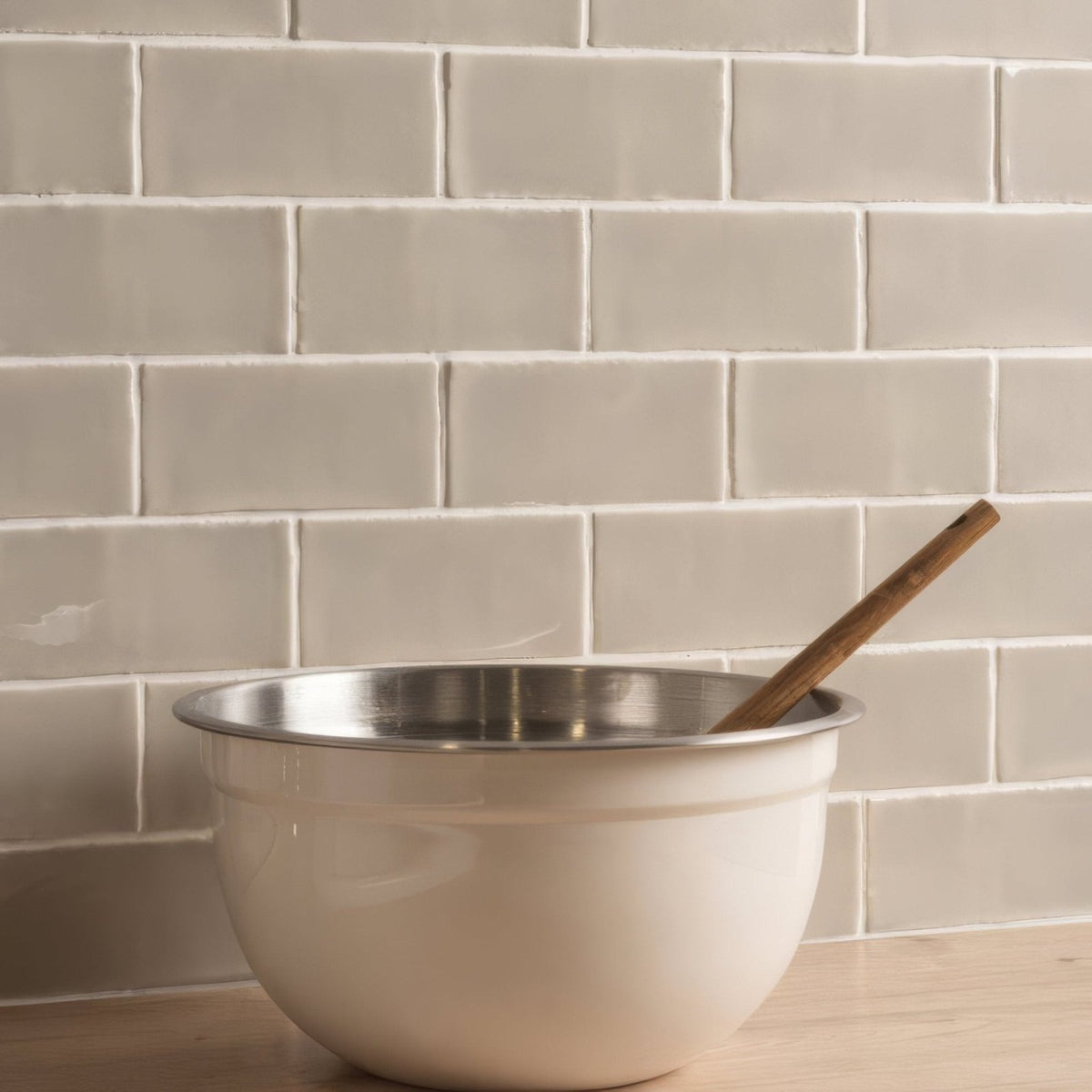 Cream-colored enamel mixing bowl with stainless steel rim and wooden spoon inside for pumice half tile wall tiles use