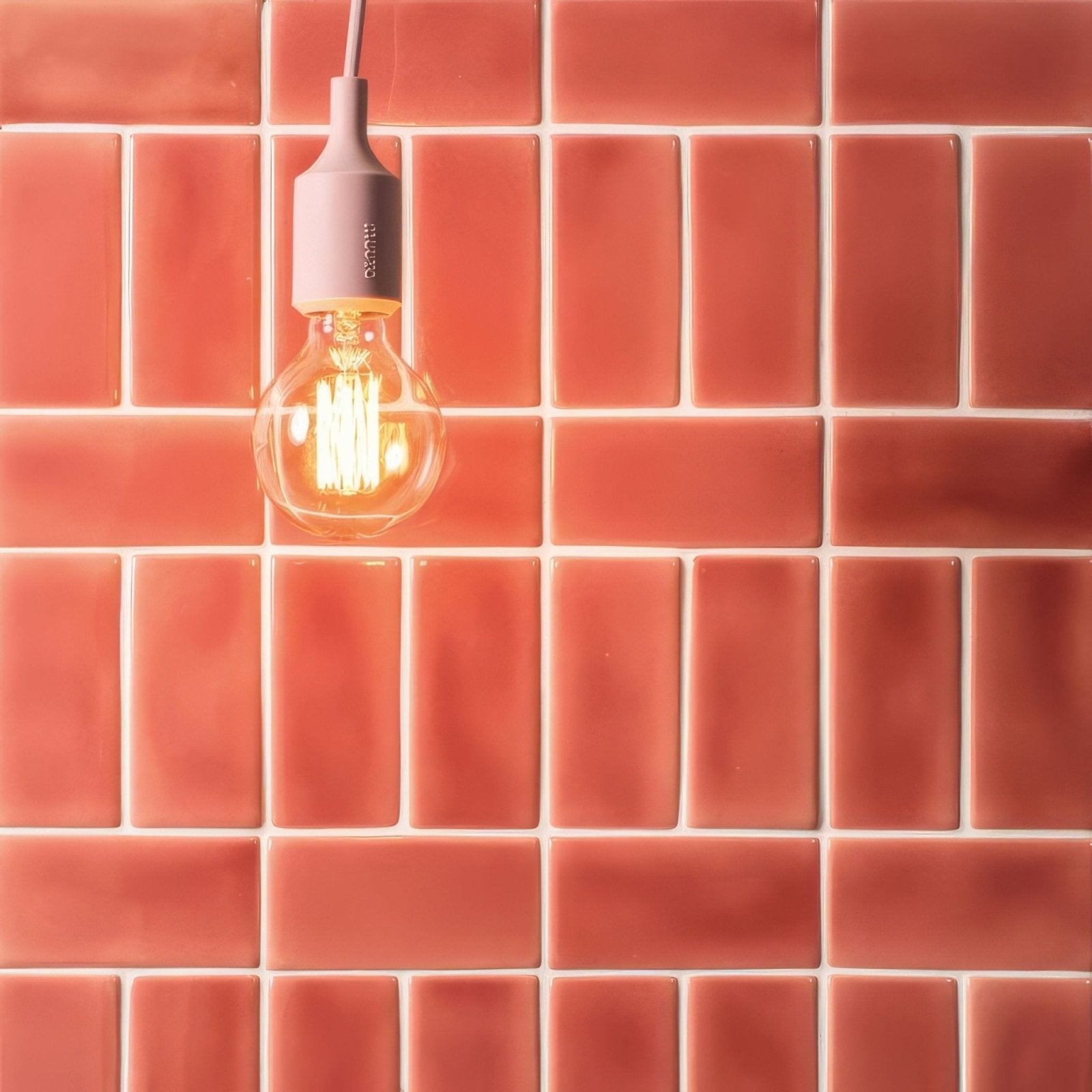 A warm-toned edison bulb with a matte pink ceramic base hanging against raspberry half tile terracotta backdrop