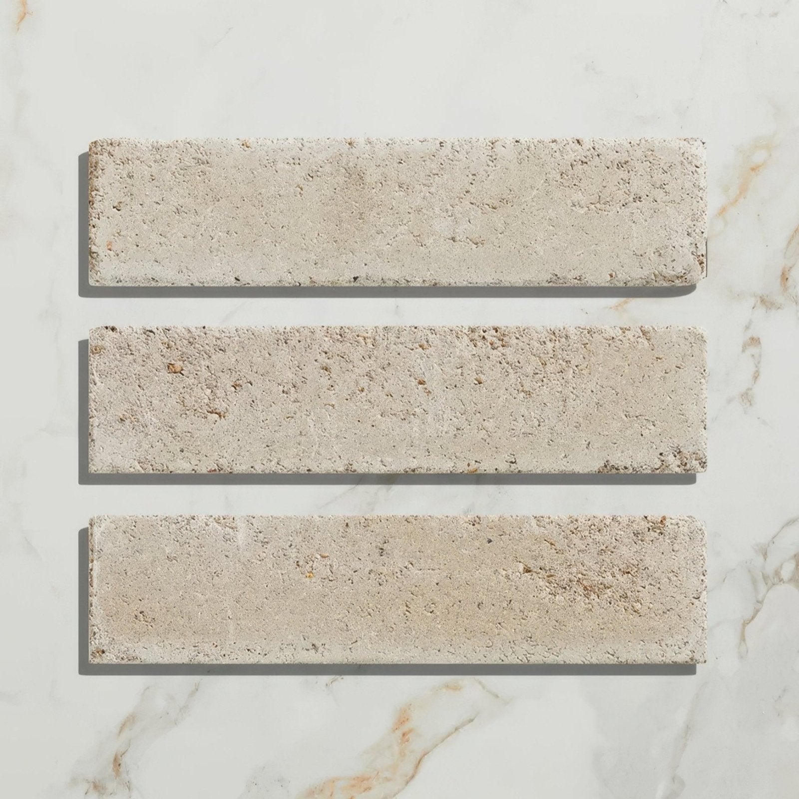 Three rectangular beige reform composite stone tumbled bianco tiles with textured rustic surface