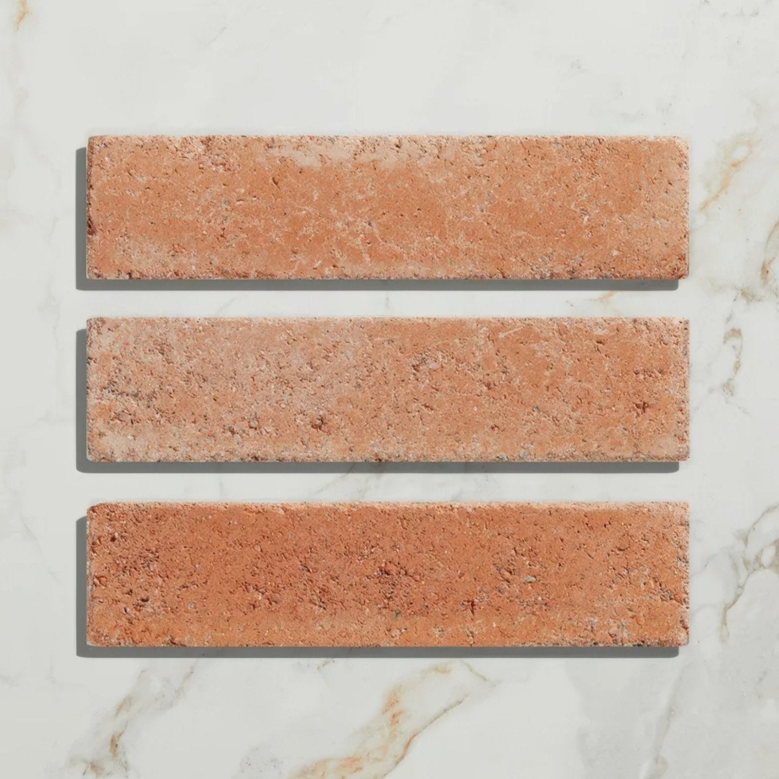 Three rectangular terracotta-colored reform composite stone tumbled cotto ceramic tiles with a rustic textured surface