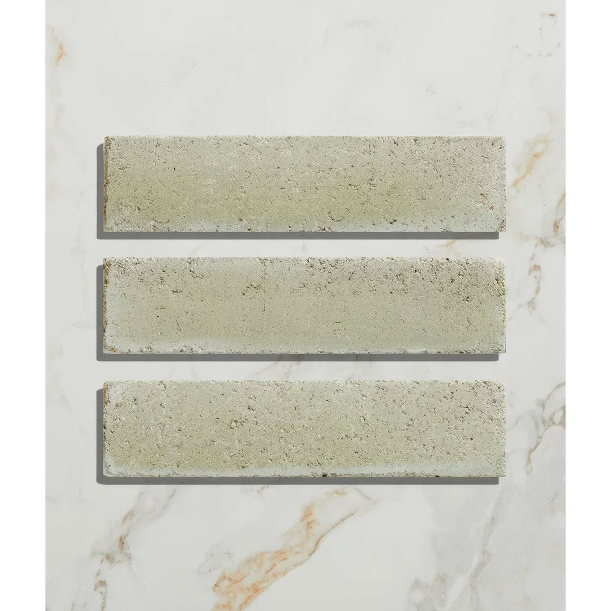 Three light gray reform composite stone tumbled mint concrete tiles with textured surface on marble background