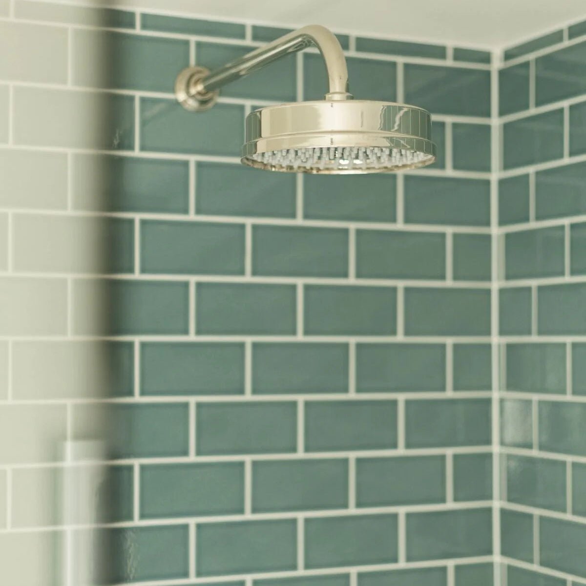Shiny chrome showerhead with circular design and multiple nozzles paired with retro metro green park glazed tile