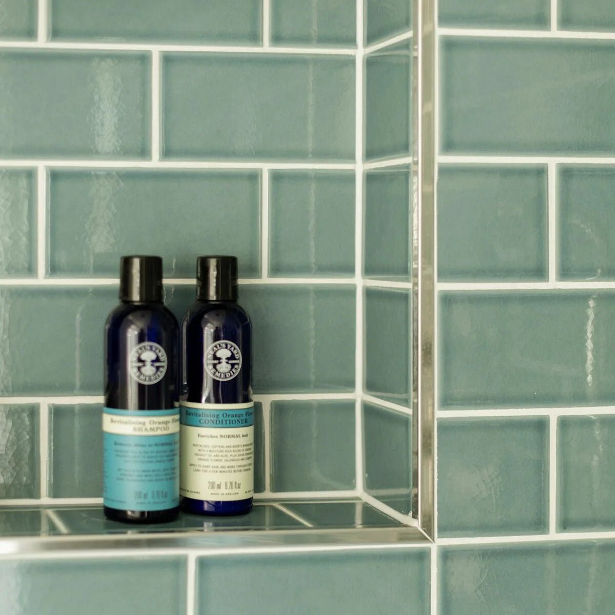 Two dark blue natura siberica shampoo and conditioner bottles with black caps on retro metro green park glazed tile