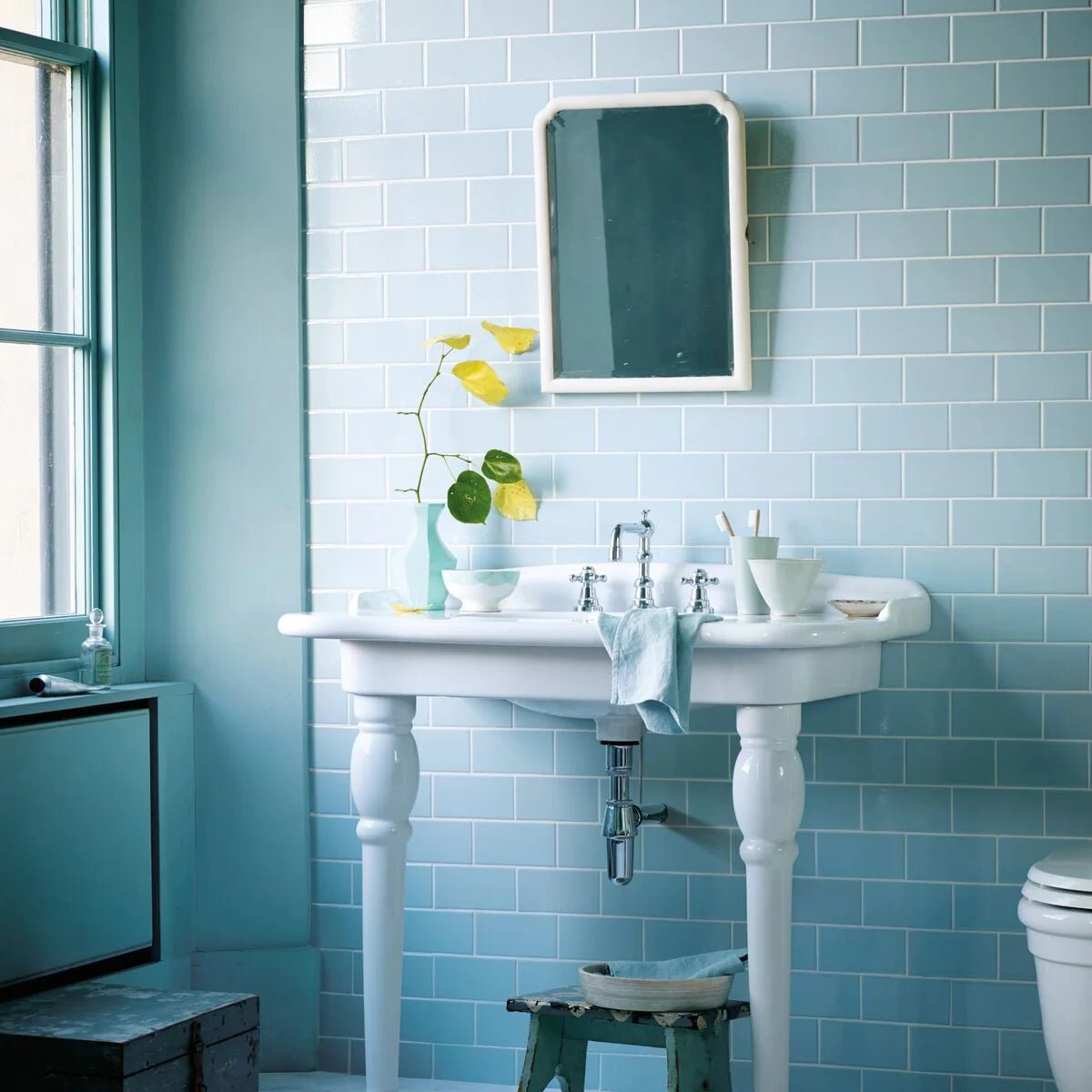 White ceramic pedestal sink with ornate turned legs and classic faucet design paired with retro metro lido blue glazed tile