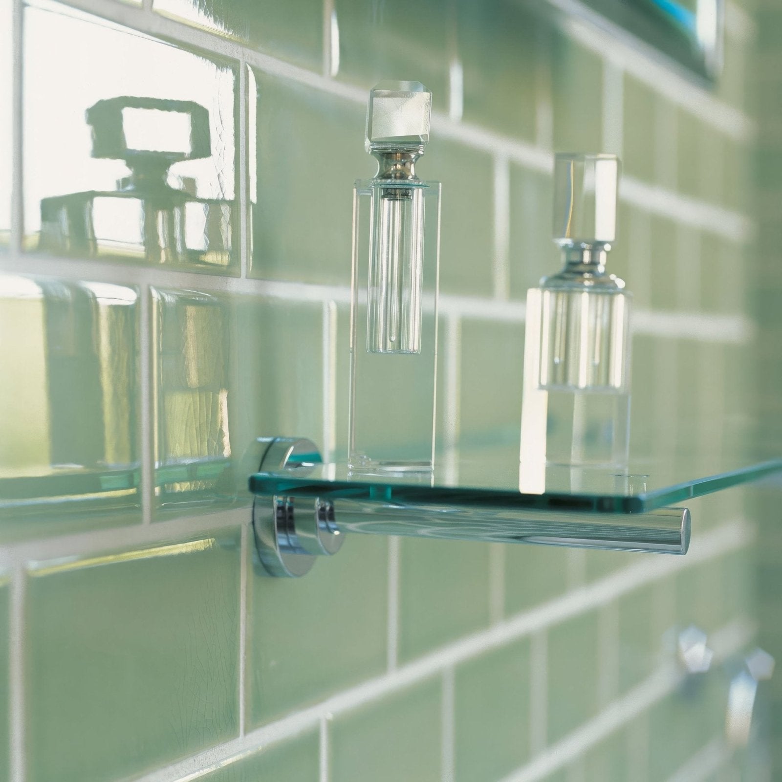Two clear glass perfume bottles with silver faceted caps on a transparent glass shelf against retro metro lime house tile