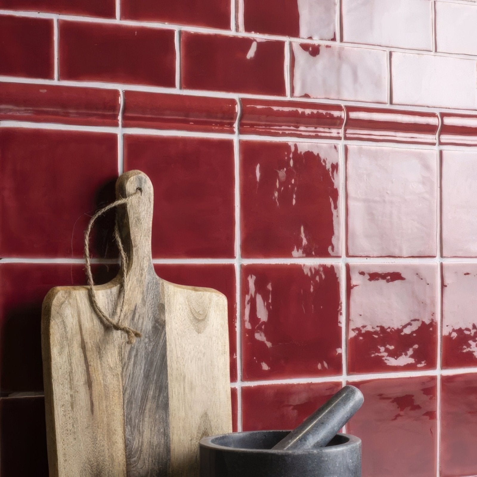 A rustic wooden cutting board with natural wood grain and rope handle leaning against red rioja half tile wall tiles