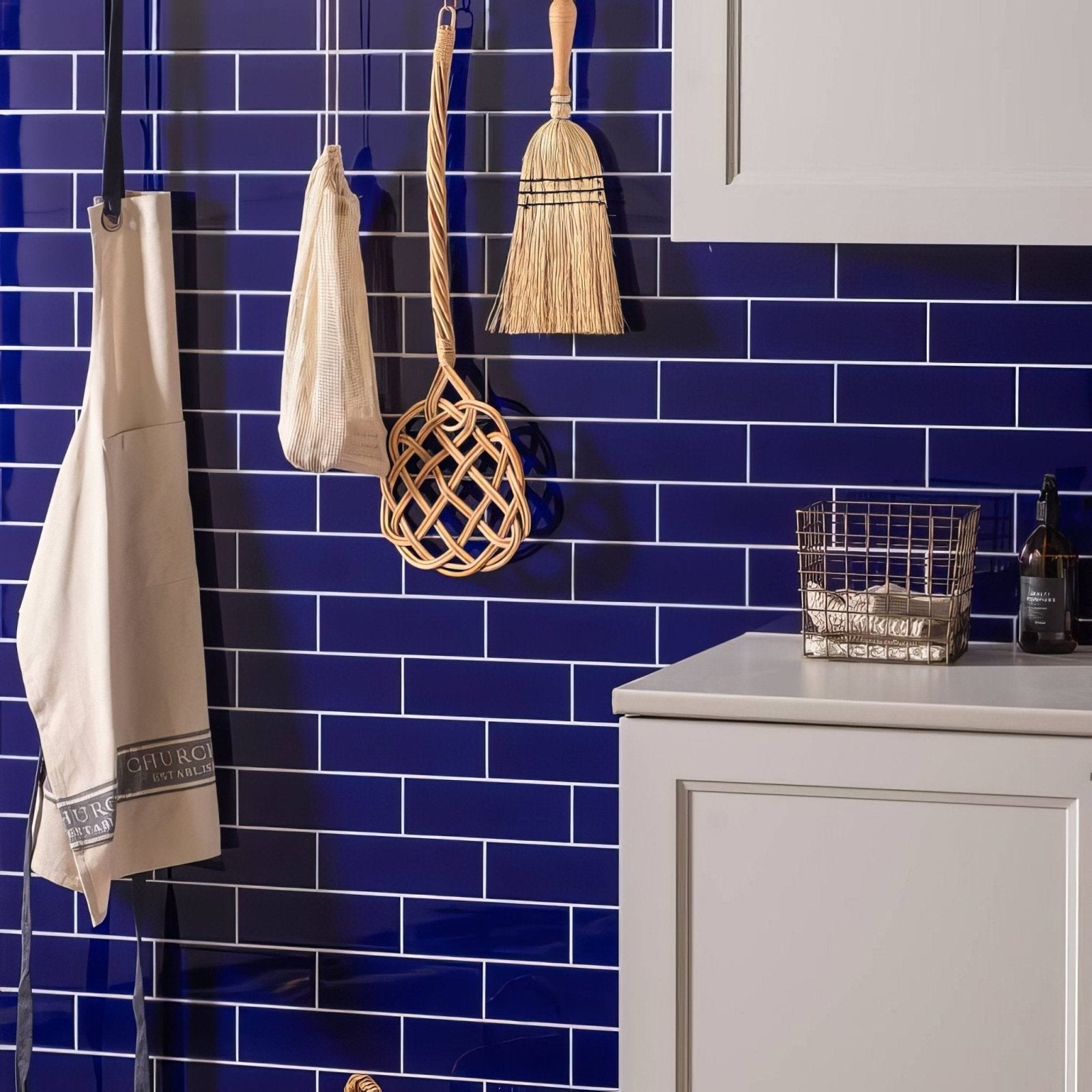 Beige apron with subtle black embroidered logo hanging against vibrant royal blue large brick tiled wall