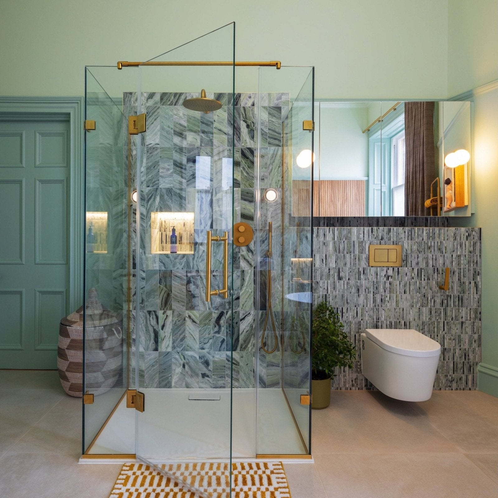Modern glass shower enclosure with gold hardware and seaspray green marble tile in herringbone pattern interior