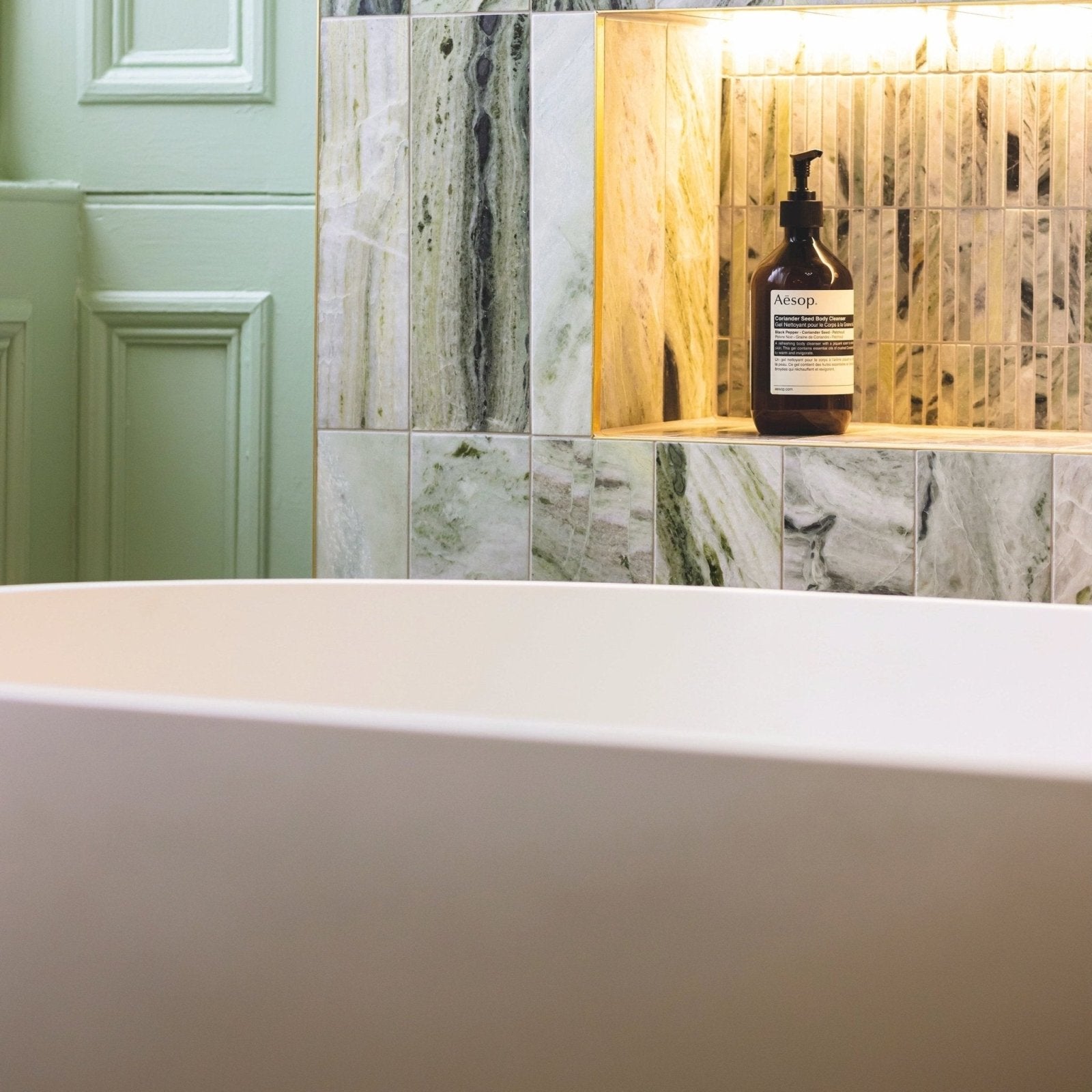 Dark amber glass bottle with black pump and white label featuring aesop brand on seaspray green marble tile 10 x 30cm