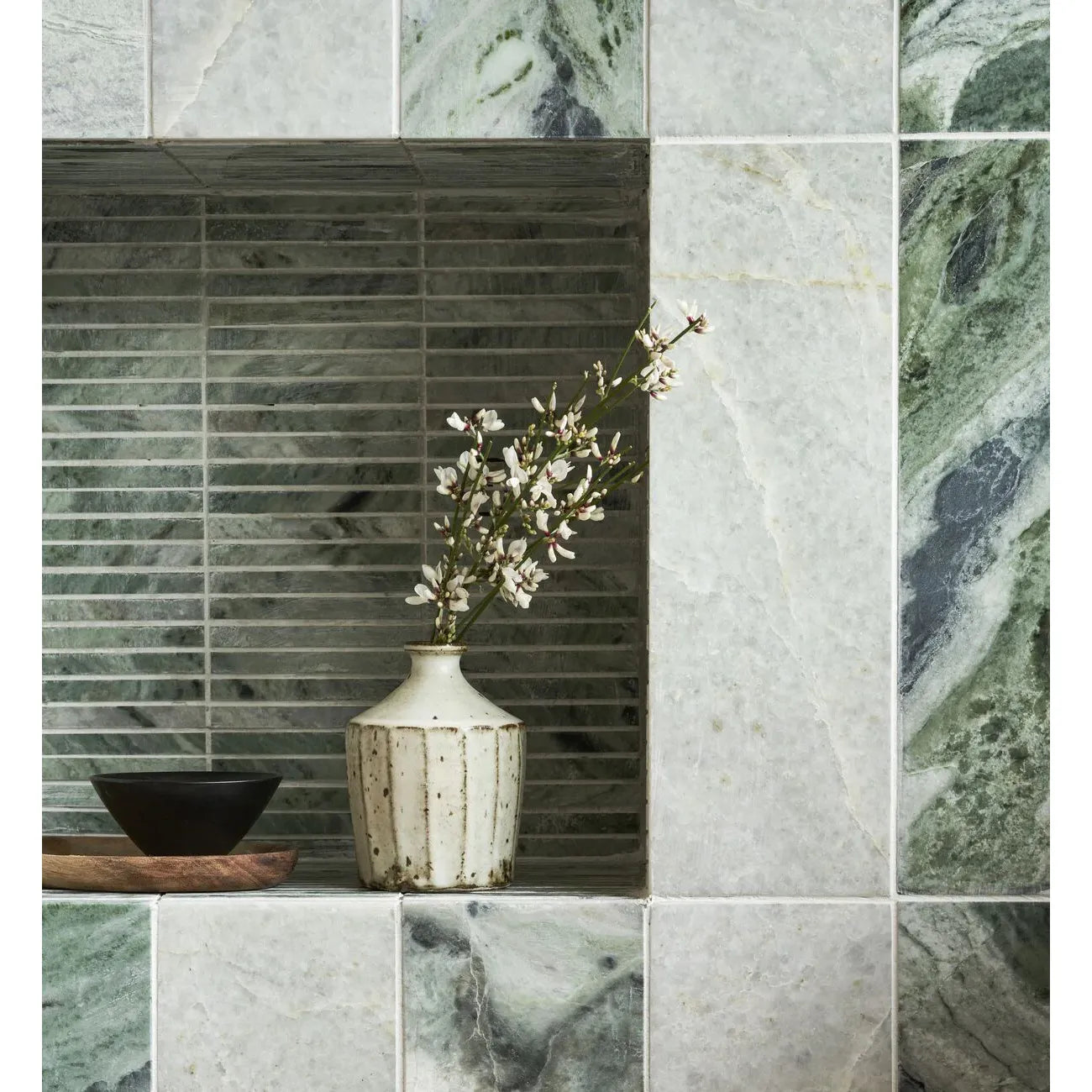 A white ceramic vase with vertical ridges and subtle speckles holding delicate white flowers in seaspray green stacked mosaic style