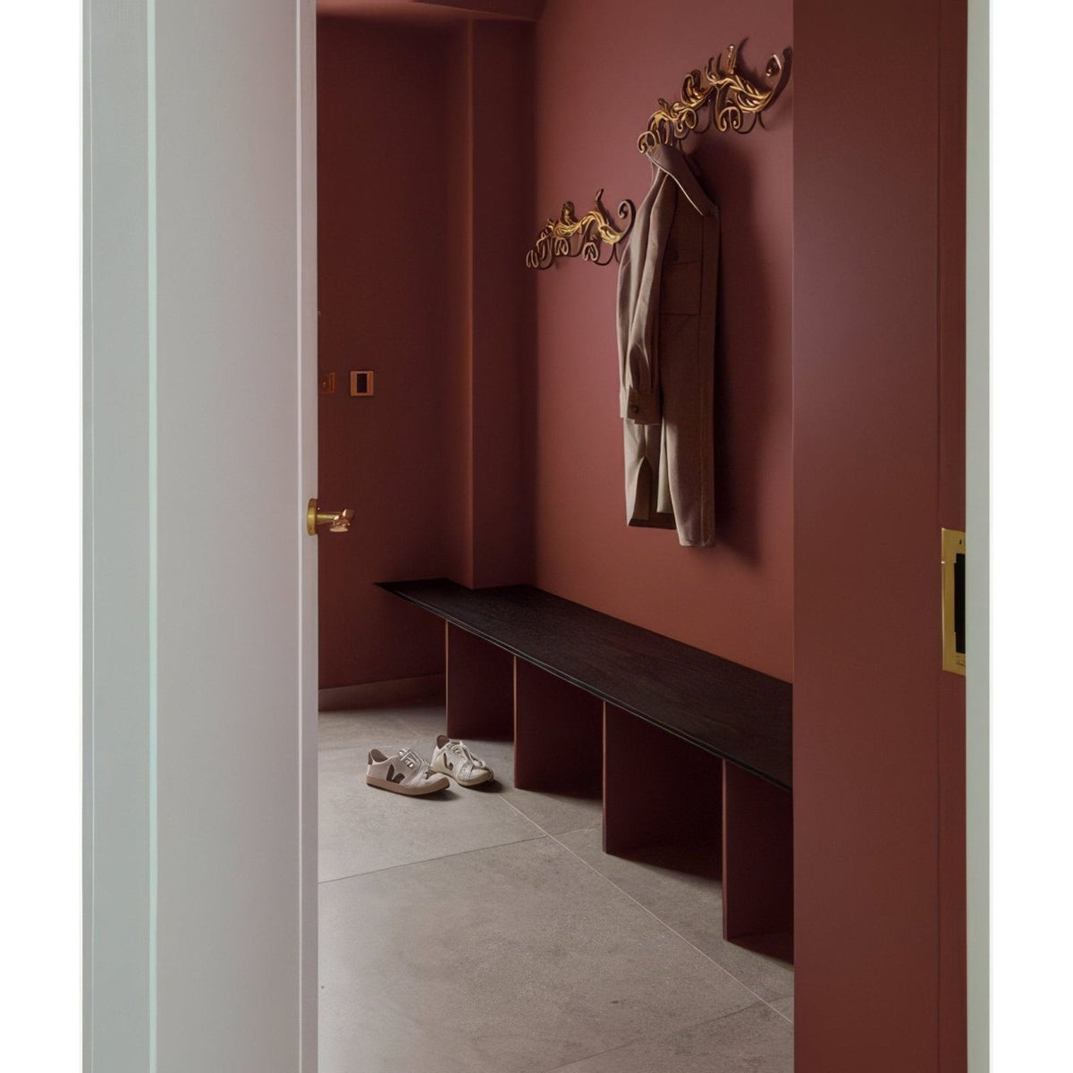 Golden ornate wall-mounted coat rack with a beige coat hanging from it in sherborne porcelain light finish