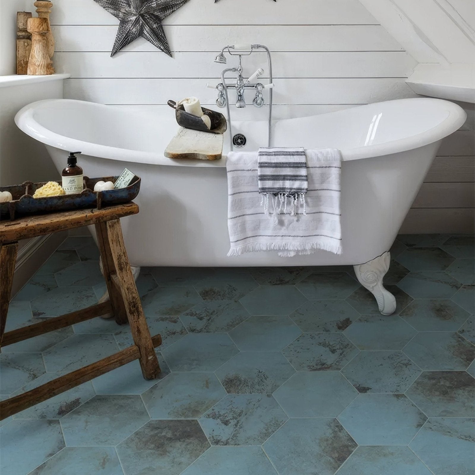 White clawfoot bathtub with chrome fixtures and a striped towel draped over the side in signature porcelain verdigris finish