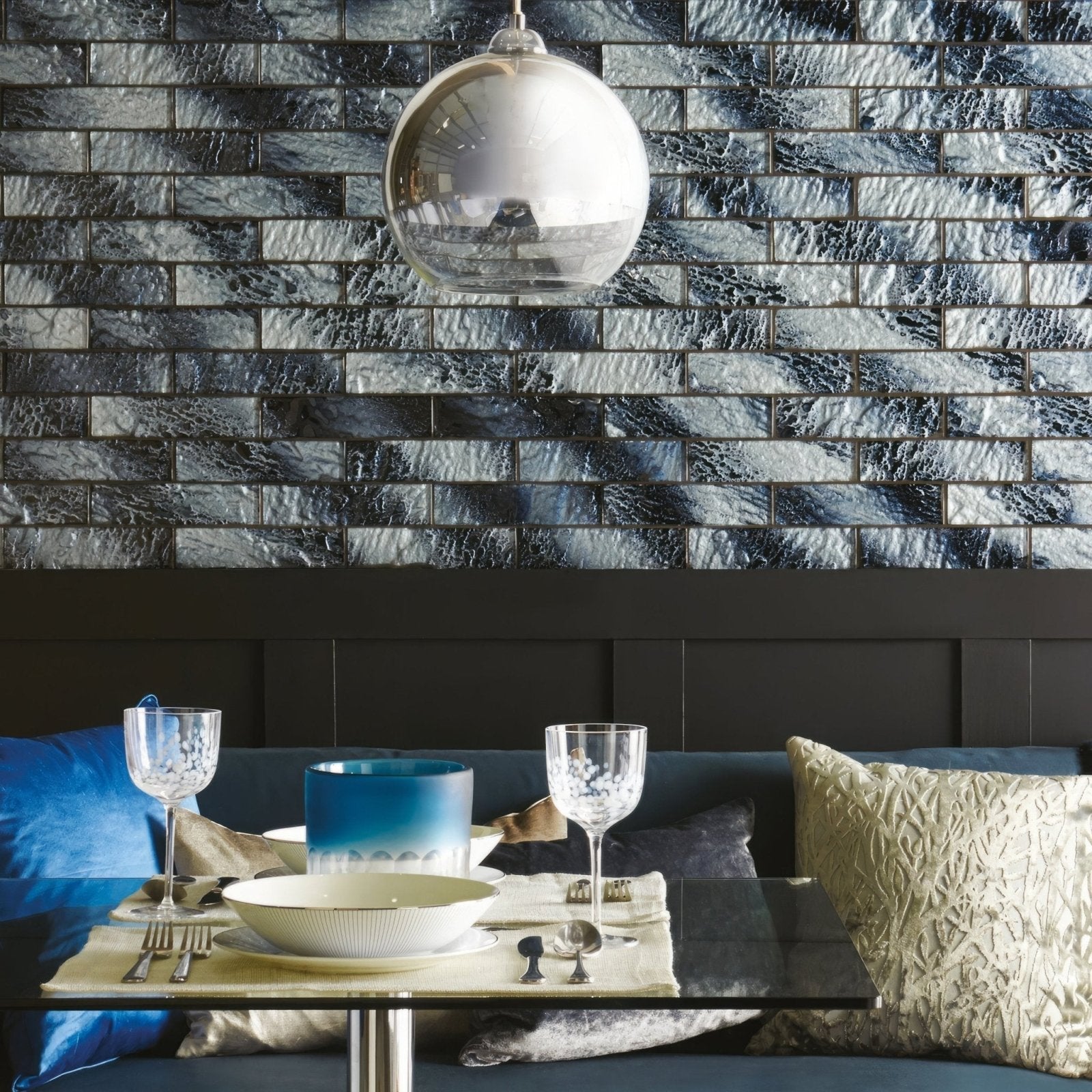 A sleek spherical glass pendant light with reflective silver finish hanging above a dining table with siva brickbond mosaic