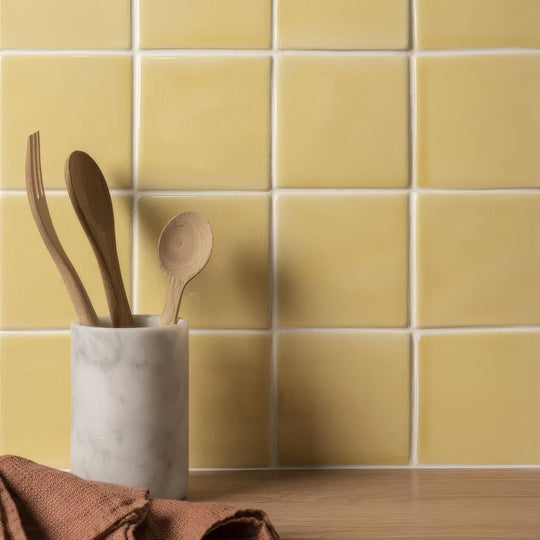 Soft yellow field tile next to a white marble utensil holder with smooth surface holding wooden spoons and forks