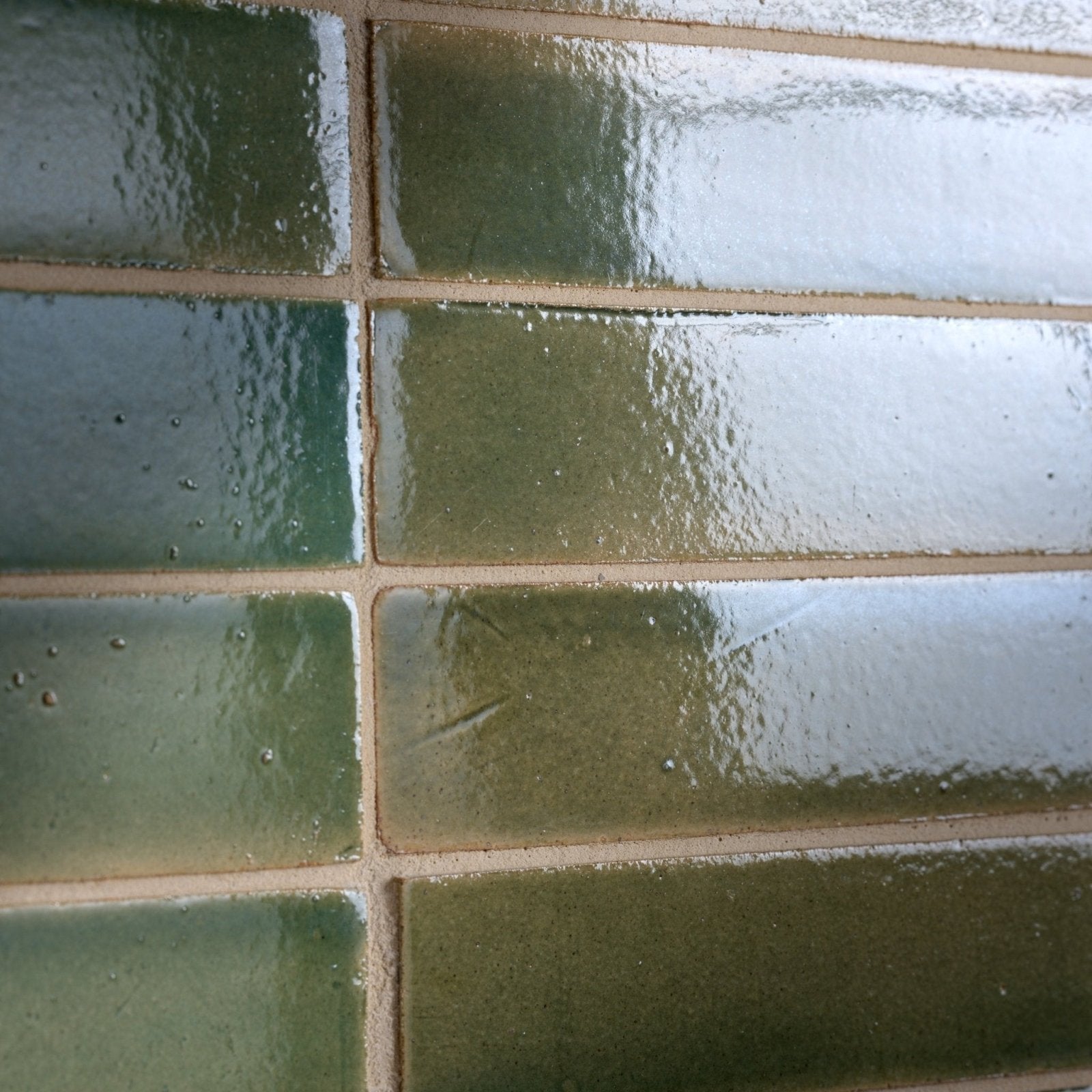 Green ceramic subway tiles with a glossy slightly textured finish and visible grout lines stone glaze ceramic olive leaf gloss brick
