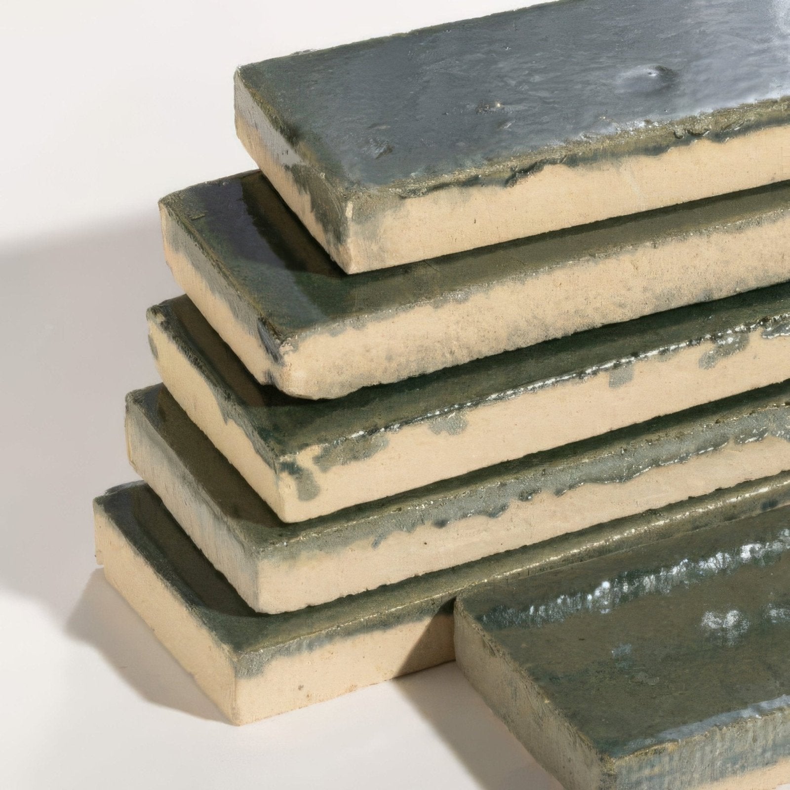 Stack of rectangular stone glaze ceramic petrol green gloss brick tiles with matte green glaze and beige clay edges