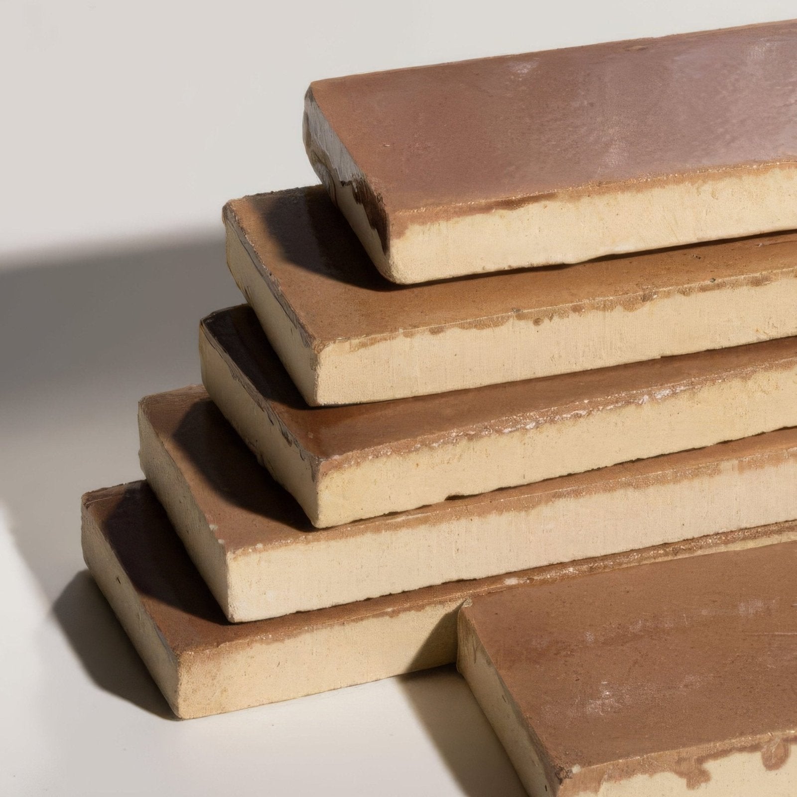 Stack of rustic brown stone glaze ceramic tan gloss brick tiles with matte finish and visible edges