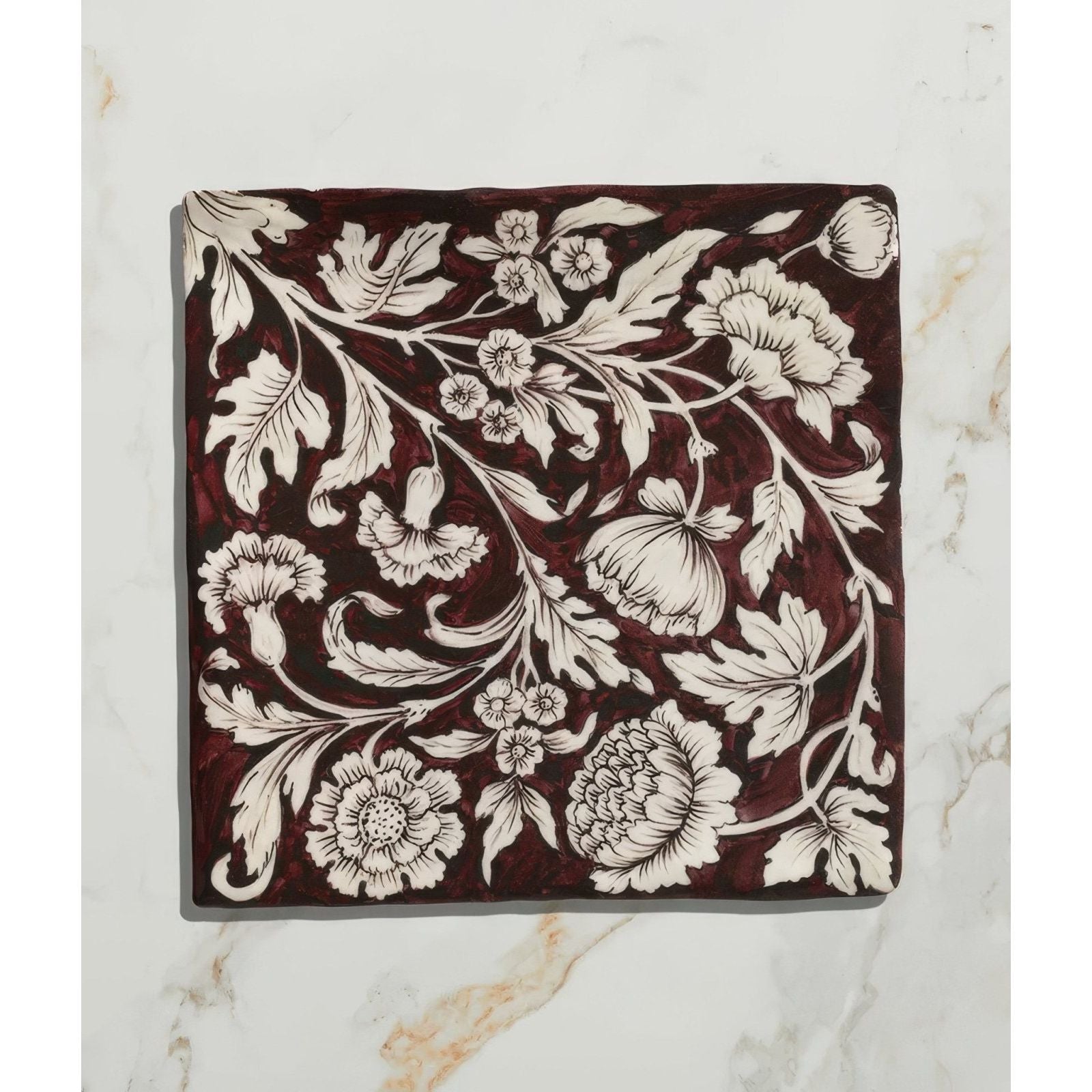 Studio Assisi Red ceramic square tile with deep burgundy glaze and intricate white floral pattern of leaves and vines