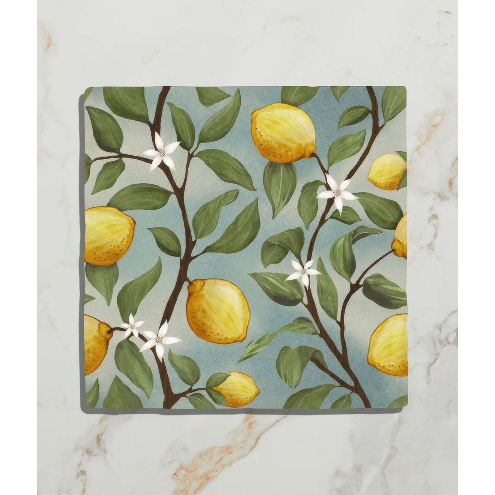 Square ceramic coaster from Studio Nonna’s Kitchen featuring yellow lemons green leaves and white blossoms on soft blue background