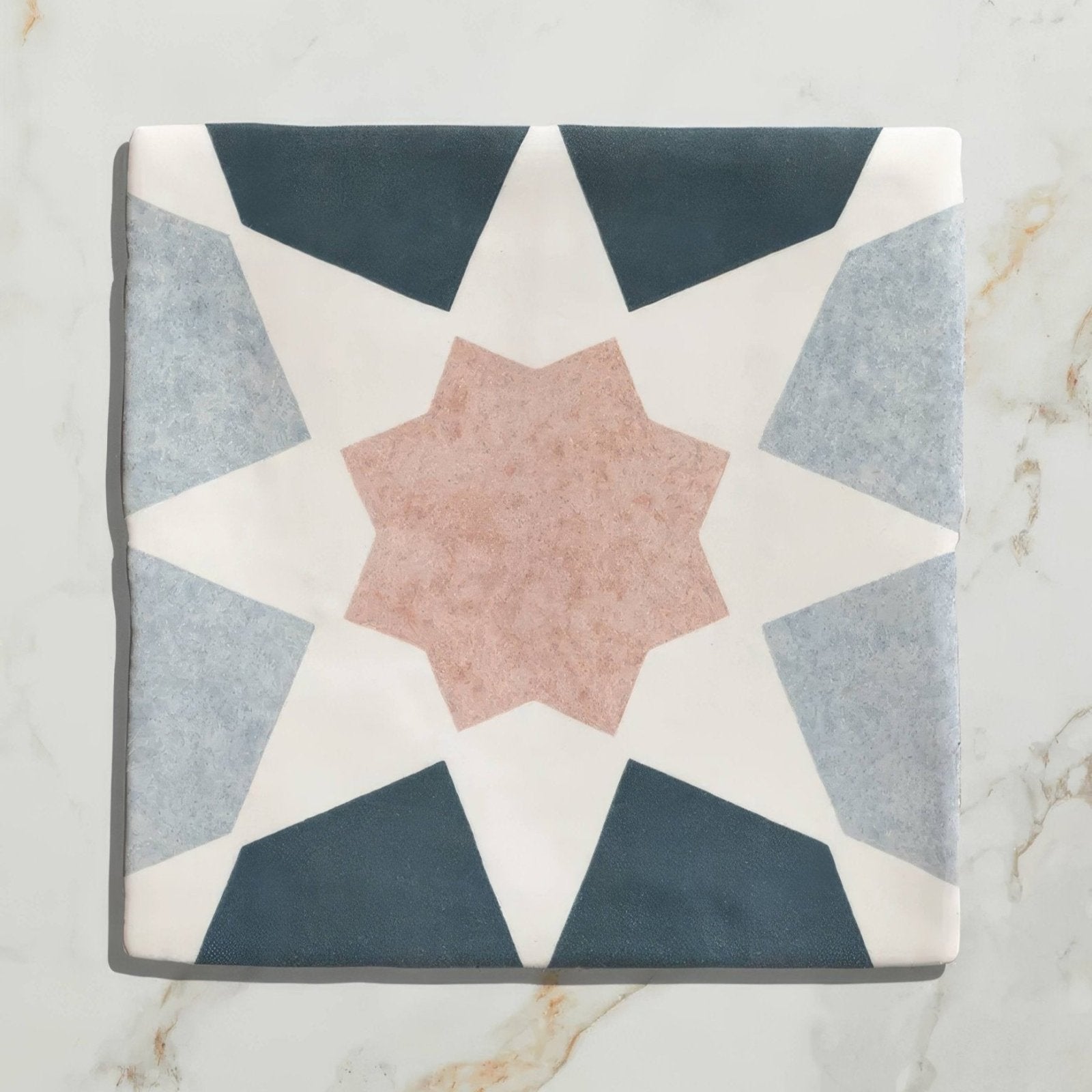 A square ceramic tile from Studio Souk featuring a geometric star pattern in navy gray and blush pink tones