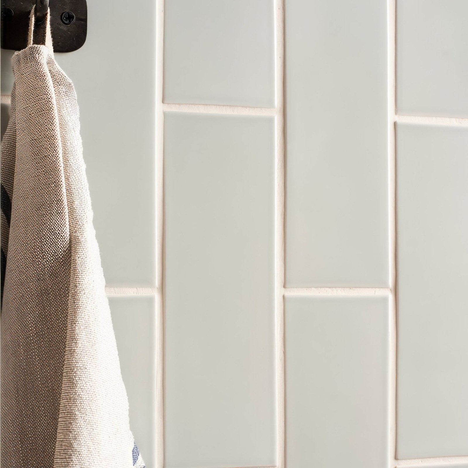 Beige woven towel hanging from a black hook against light gray brick tile sudbury subway tile wall