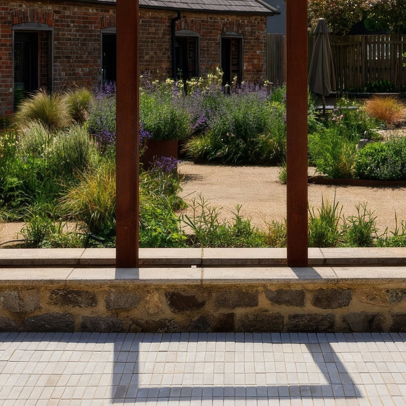 Rustic wooden pergola posts frame a sunlit garden with lavender and greenery featuring trafalgar sandstone tumbled klinkers