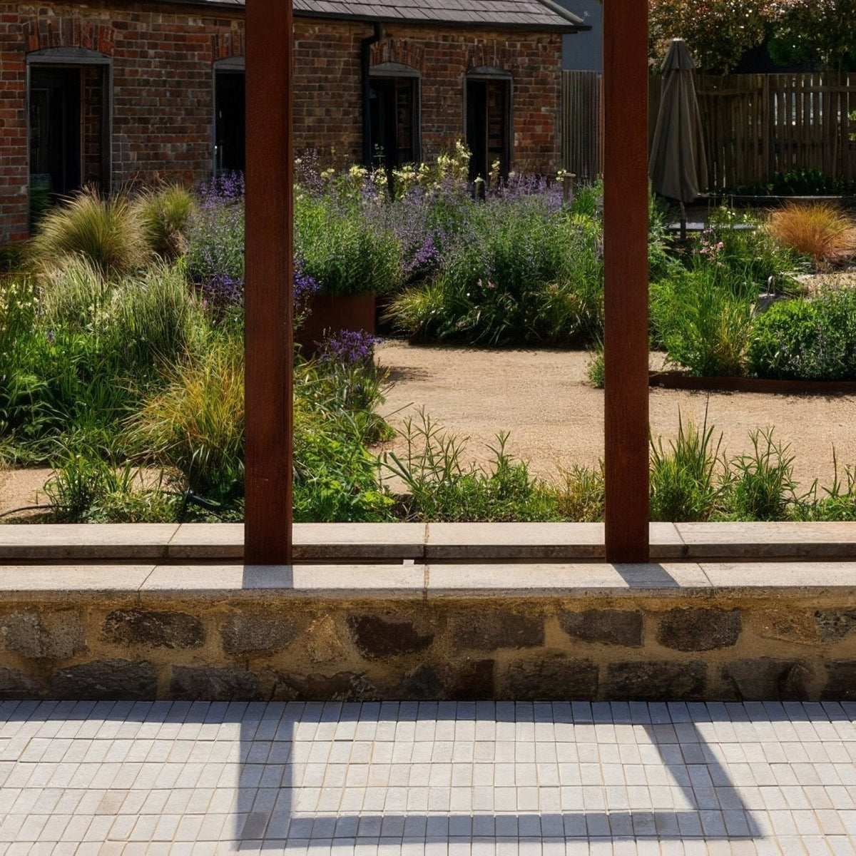 Rustic wooden pergola posts frame a sunlit garden with lavender and greenery featuring trafalgar sandstone tumbled klinkers