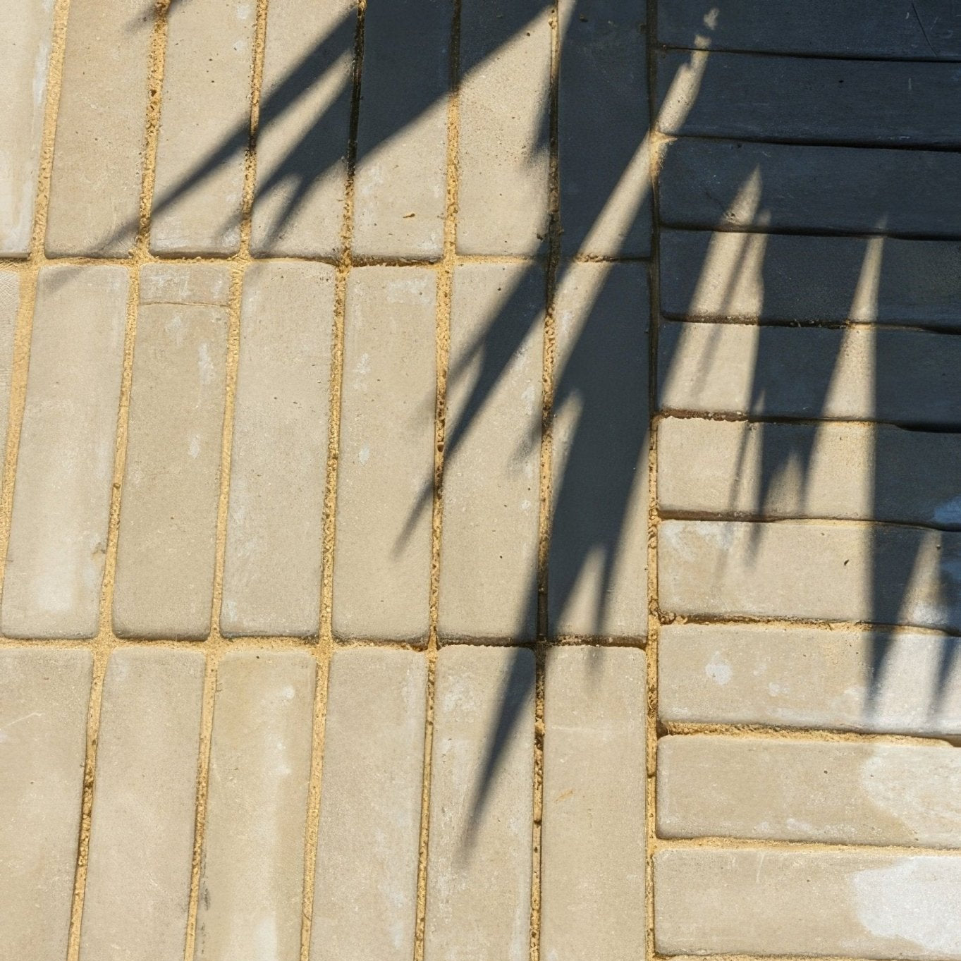 Beige rectangular trafalgar sandstone tumbled klinkers arranged in a herringbone pattern next to dark gray bricks