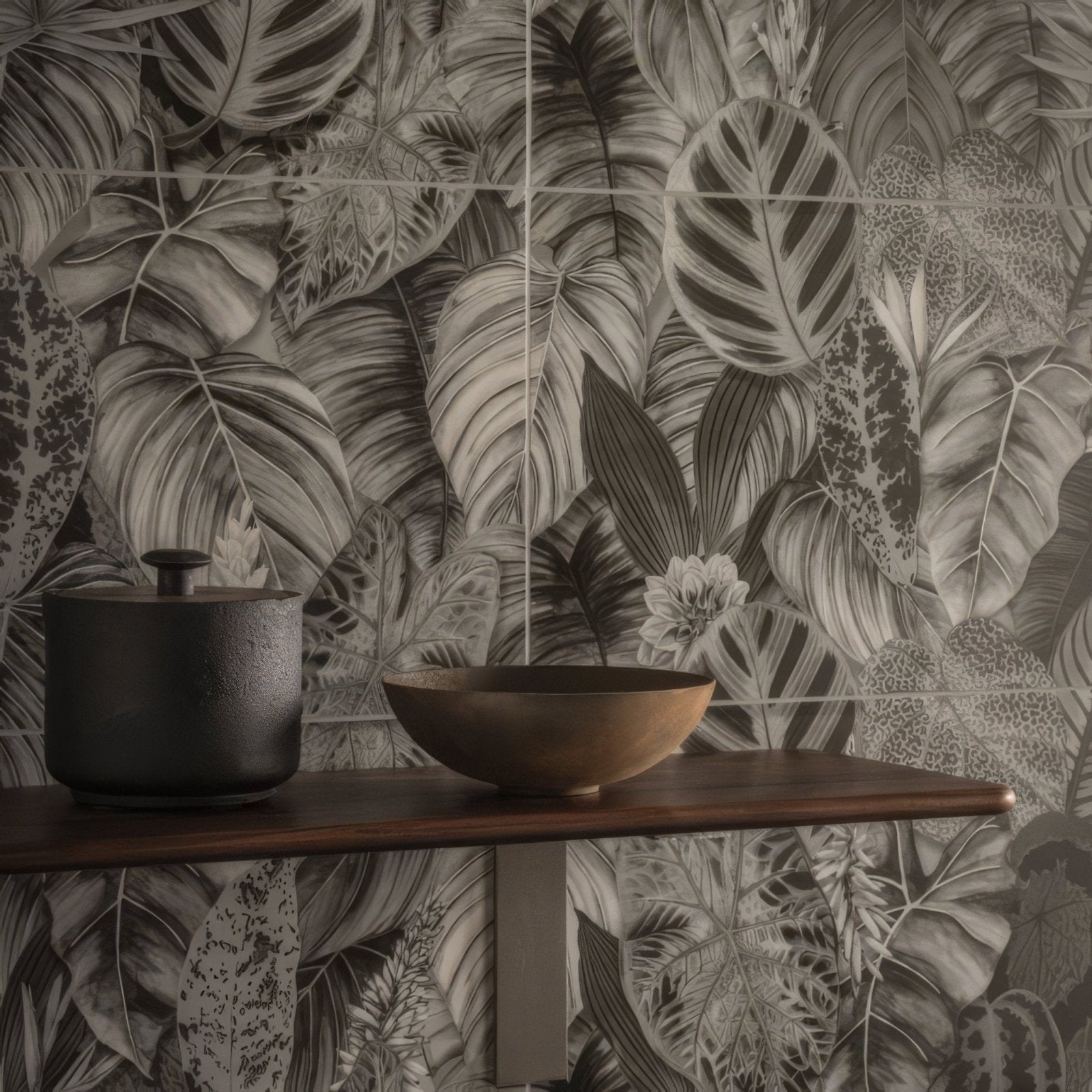 Dark matte-finished ceramic pot with small black lid beside wooden bowl on shelf in tropical oasis monochrome tile